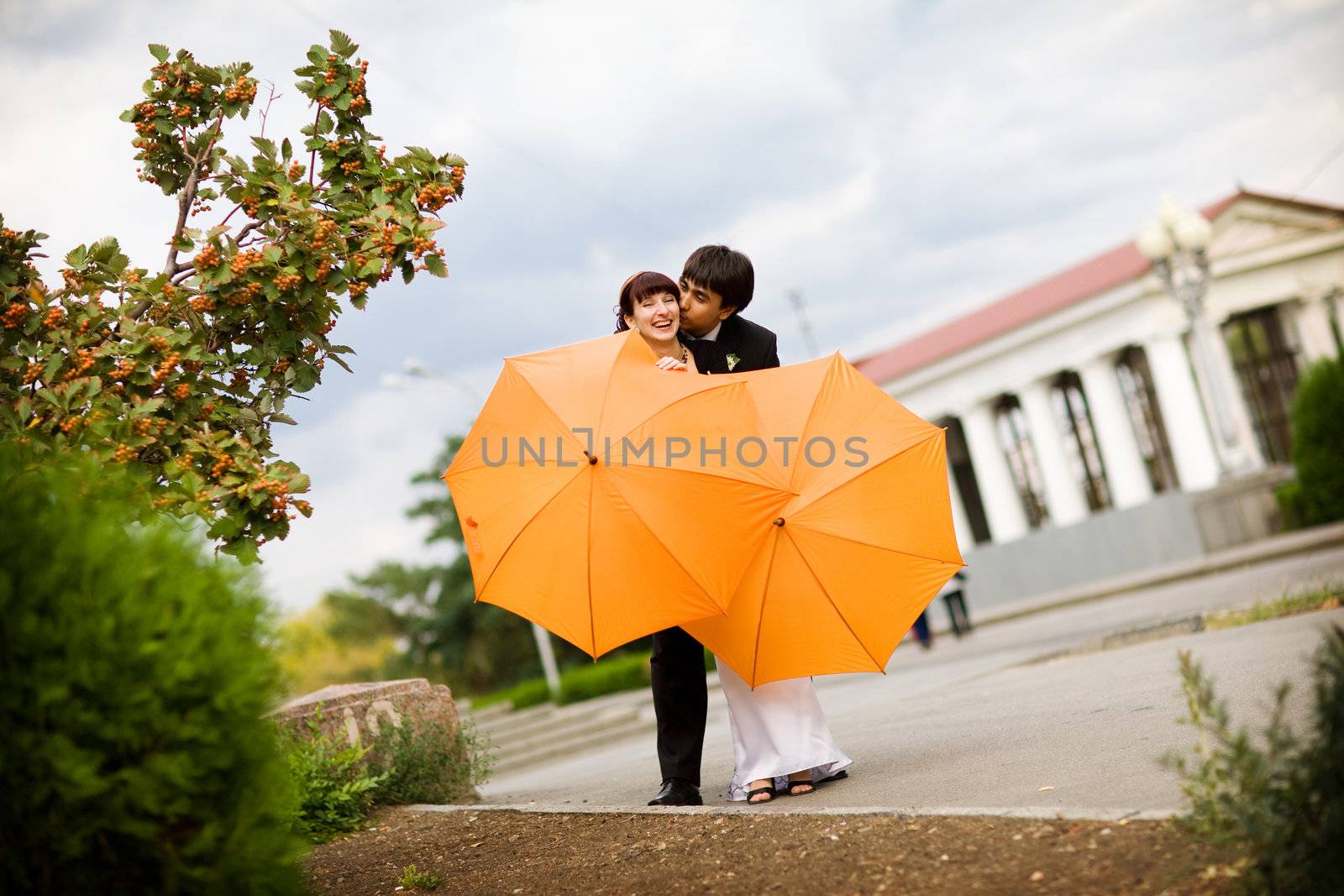 kiss of bride and groom with orange umbrellas 