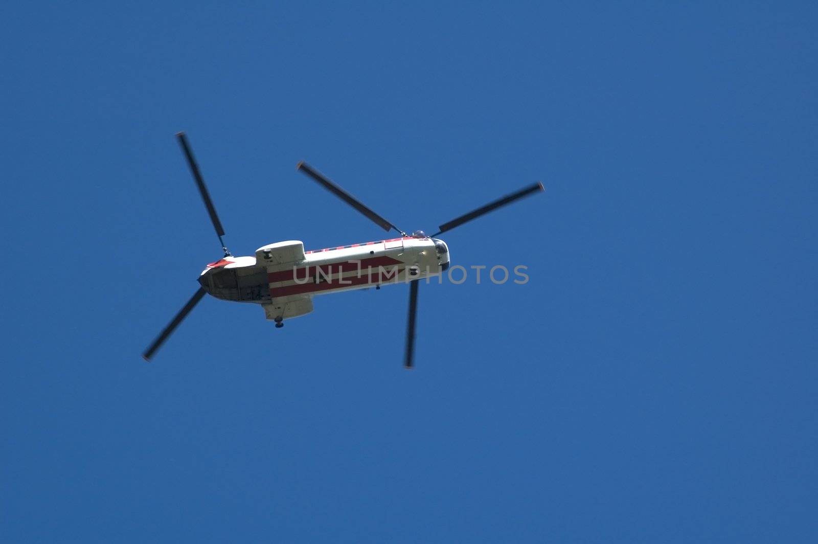 A twin rotor helicopter flying overhead against a blue sky