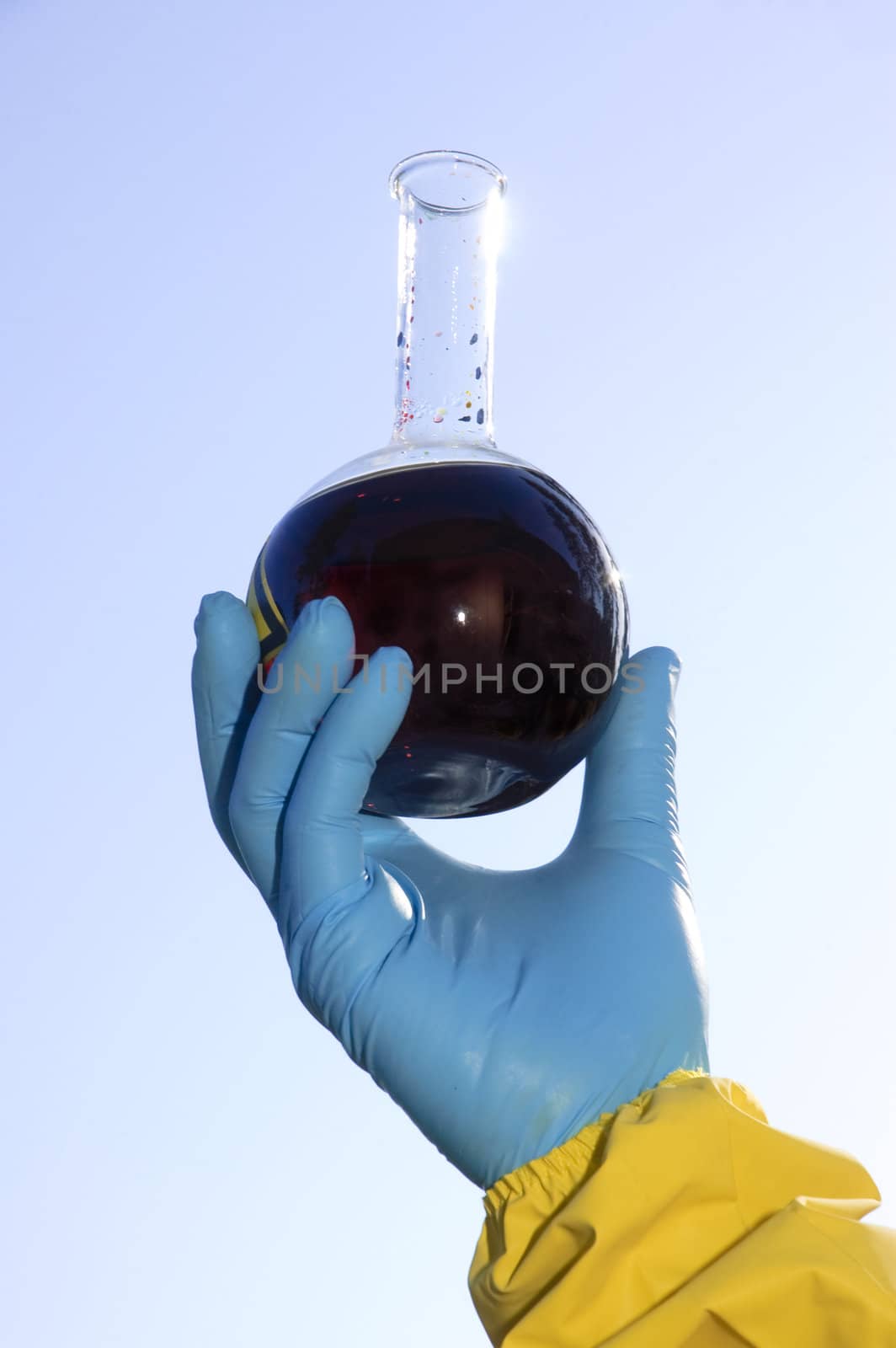 Hand wearing protective gloves and hazmat clothing holding a flask of hazardous chemical up in the air to chech the transparency