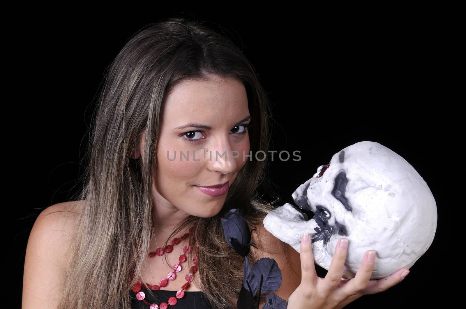 Beautiful young brunette woman holding skull and a black rose withan evil smile for halloween
