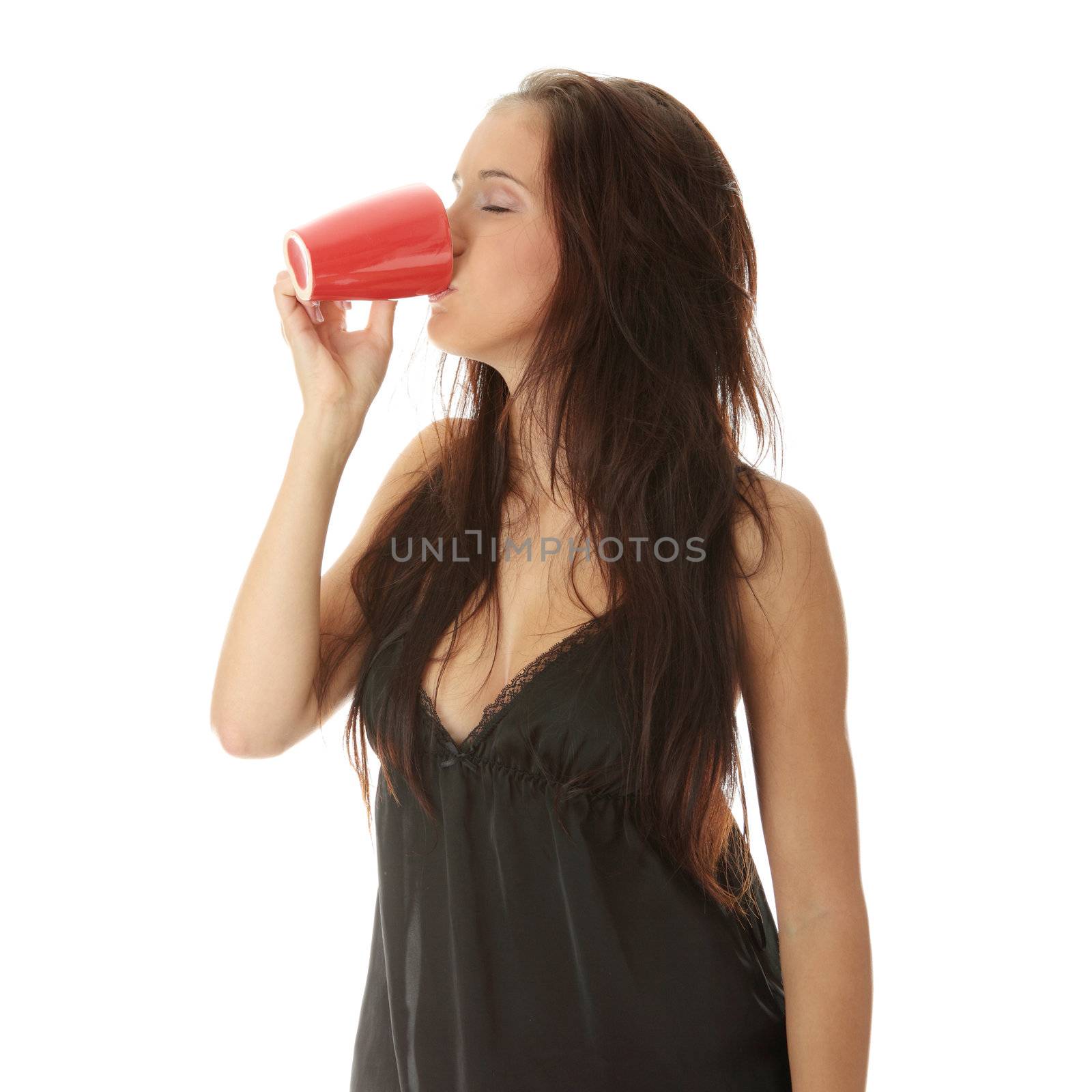 The beautiful young woman drinks morning coffee or tea from red mug