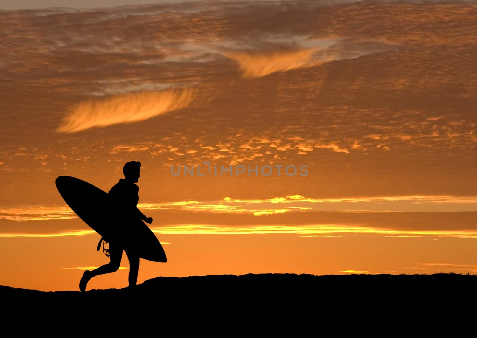 Surfer running out to sea to get the last wave in before sunset