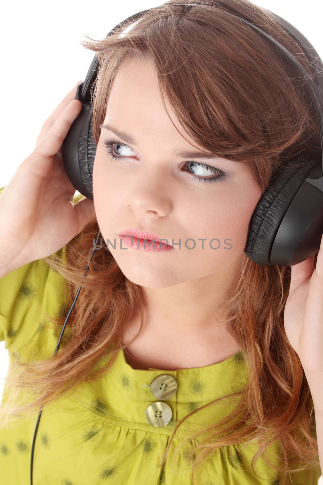 Beautiful teenage girl in a green dress listening to music with big headphones, isolated on white