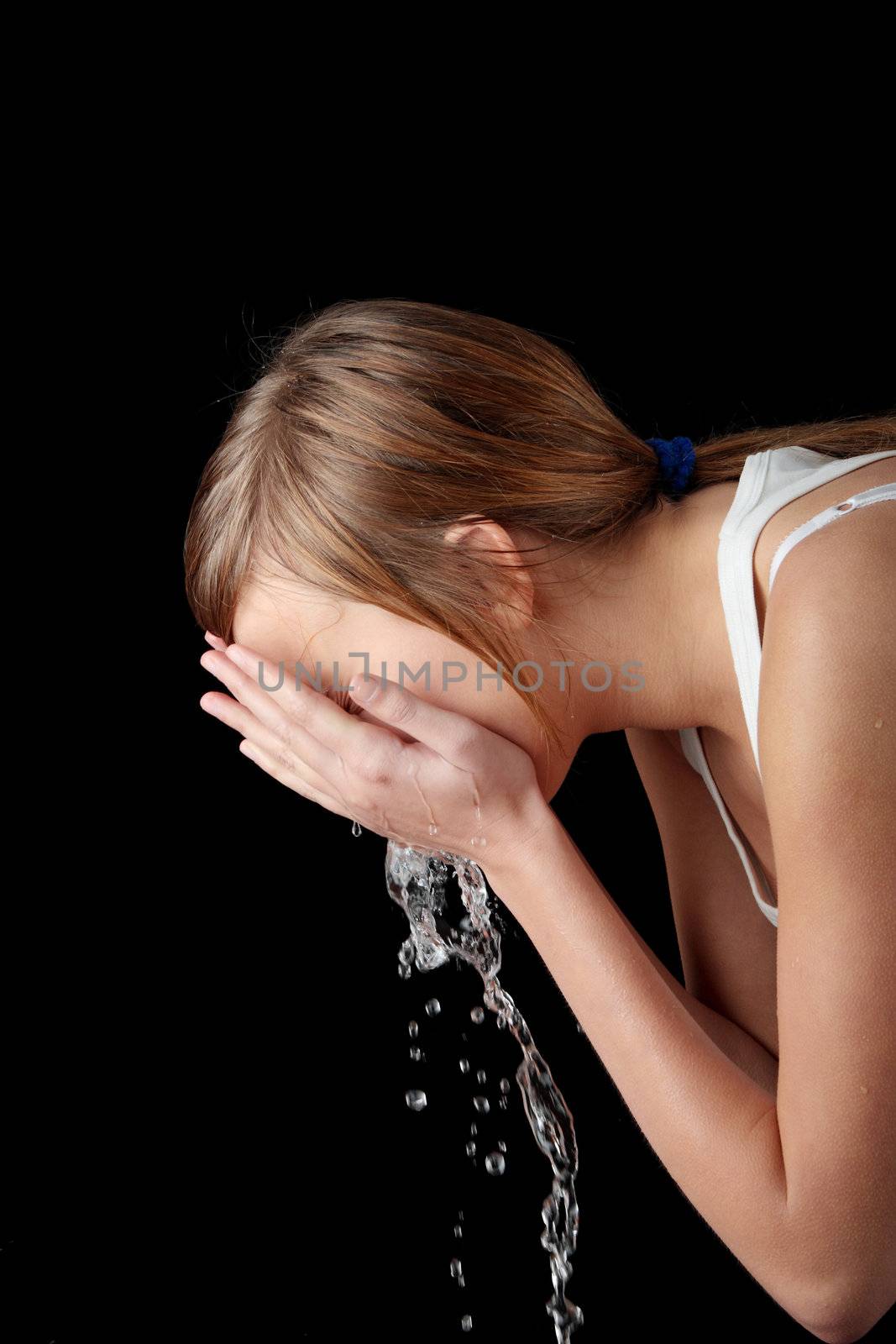Teen girl washing her face with water, isolated on black