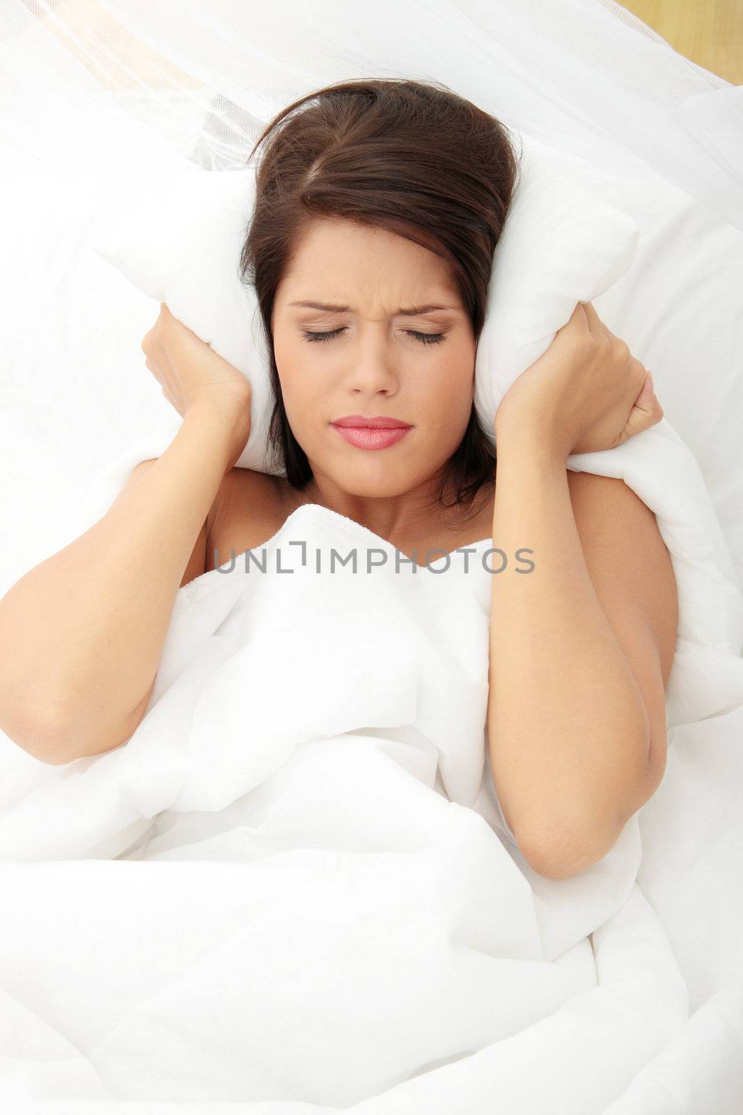 Female lying on bed and closing her ears with pillow