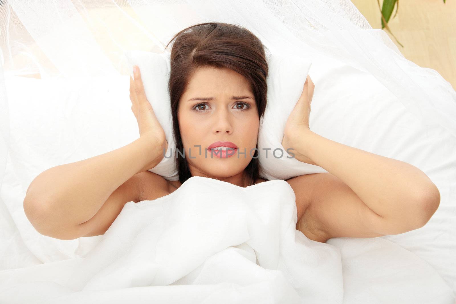 Female lying on bed and closing her ears with pillow