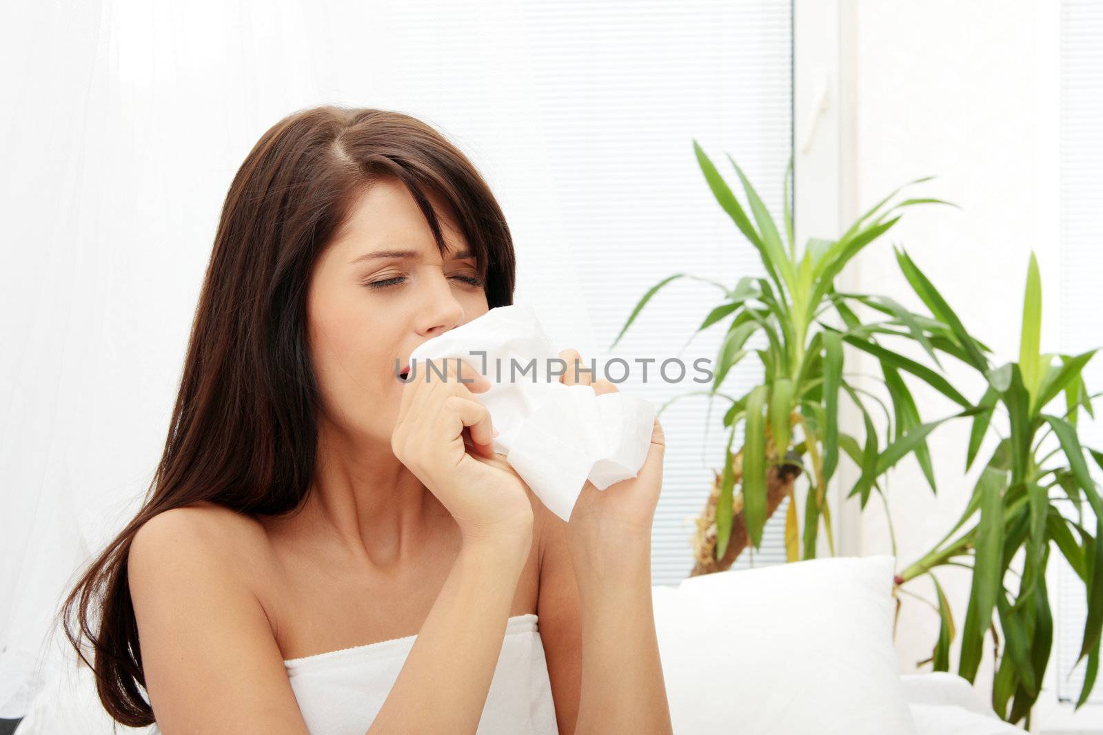 Sick woman sitting in bed with tissue and blowing her nose into it