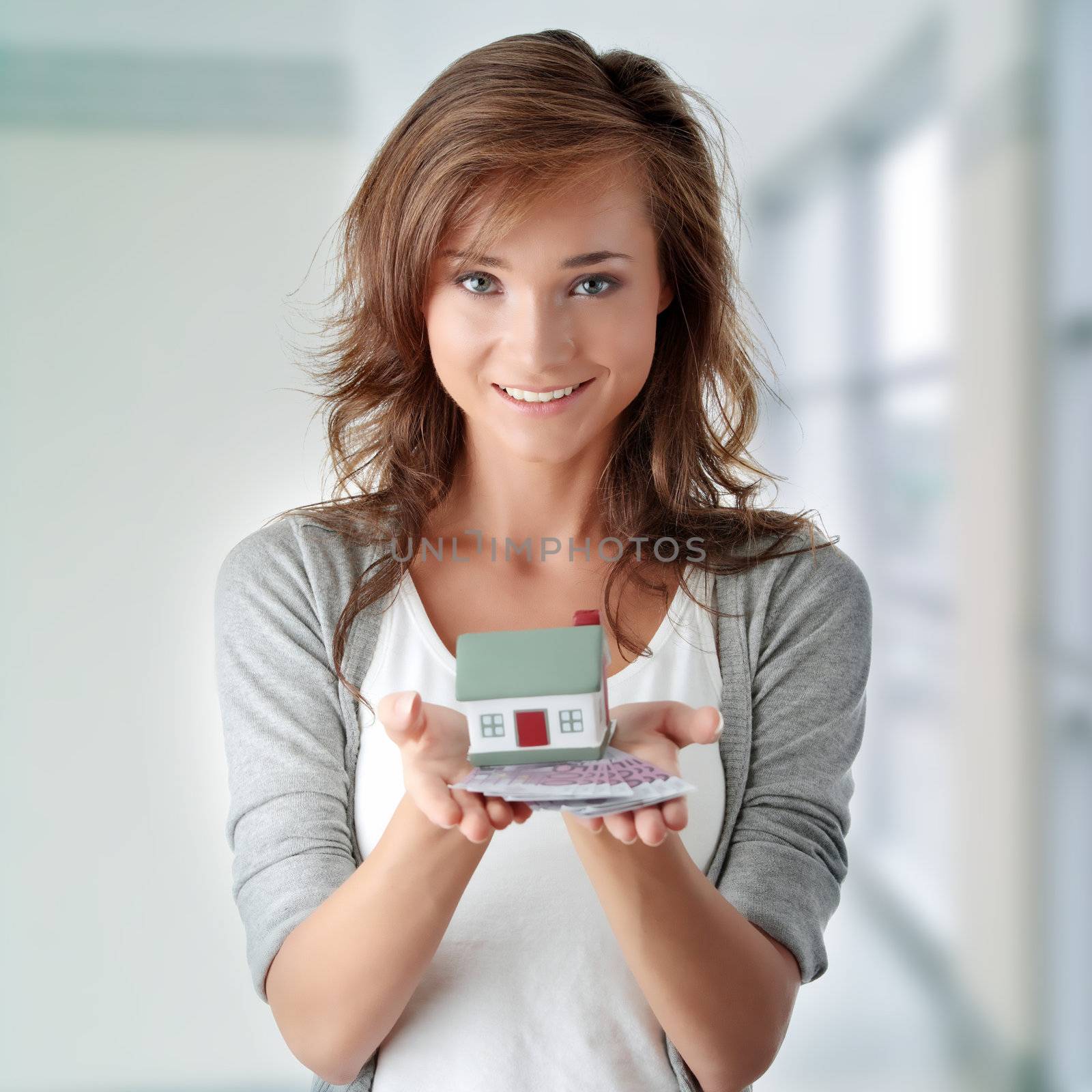 Beautiful young woman holding euros bills and house model over white - real estate loan concept