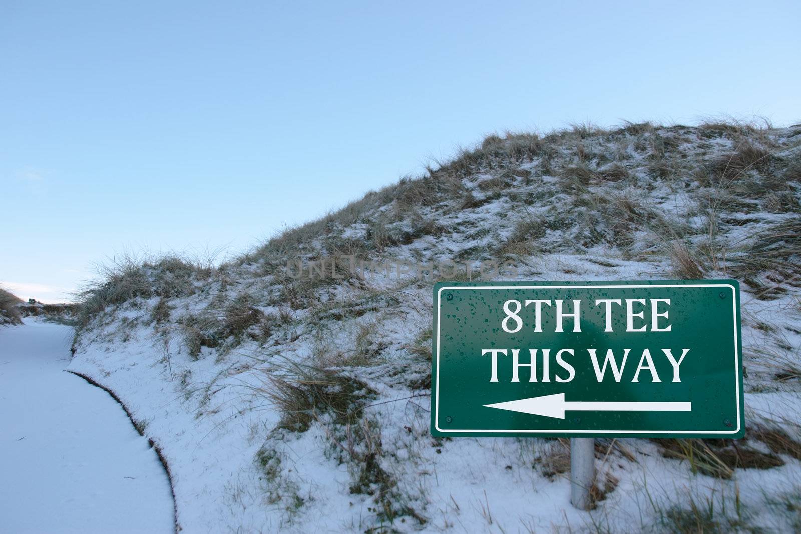8th tee this way sign on a snow covered links golf course in ireland in snowy winter weather