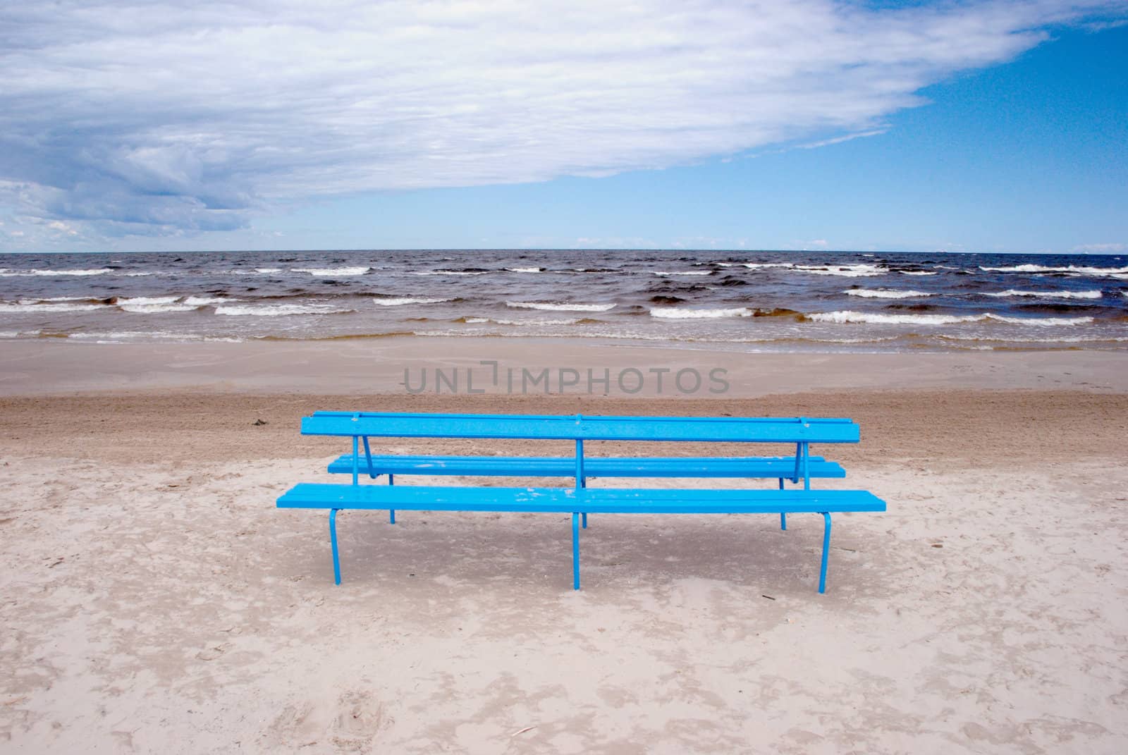 Blue bench on the beach sand near the sea.