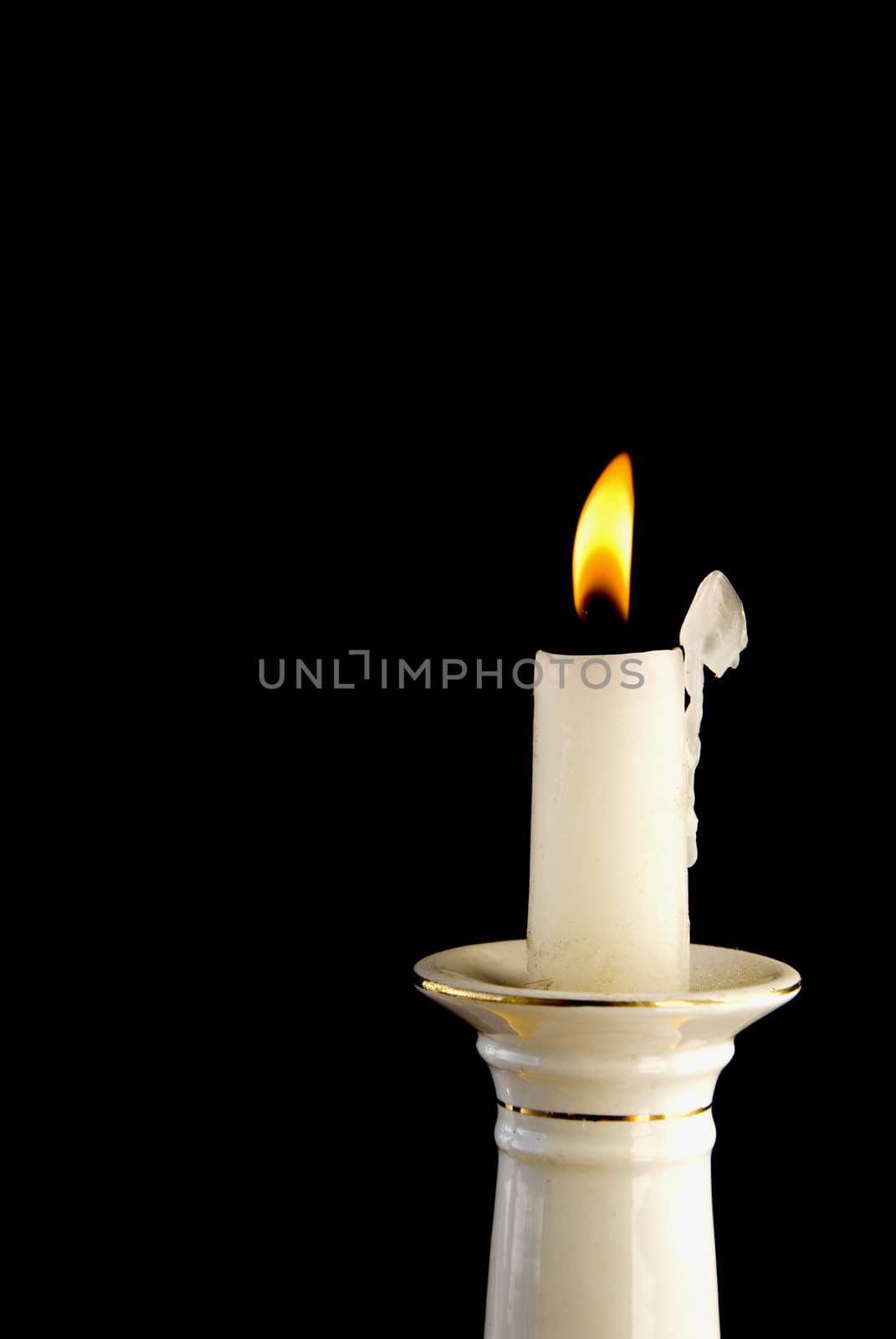 White burning candle in candlestick in the dark background