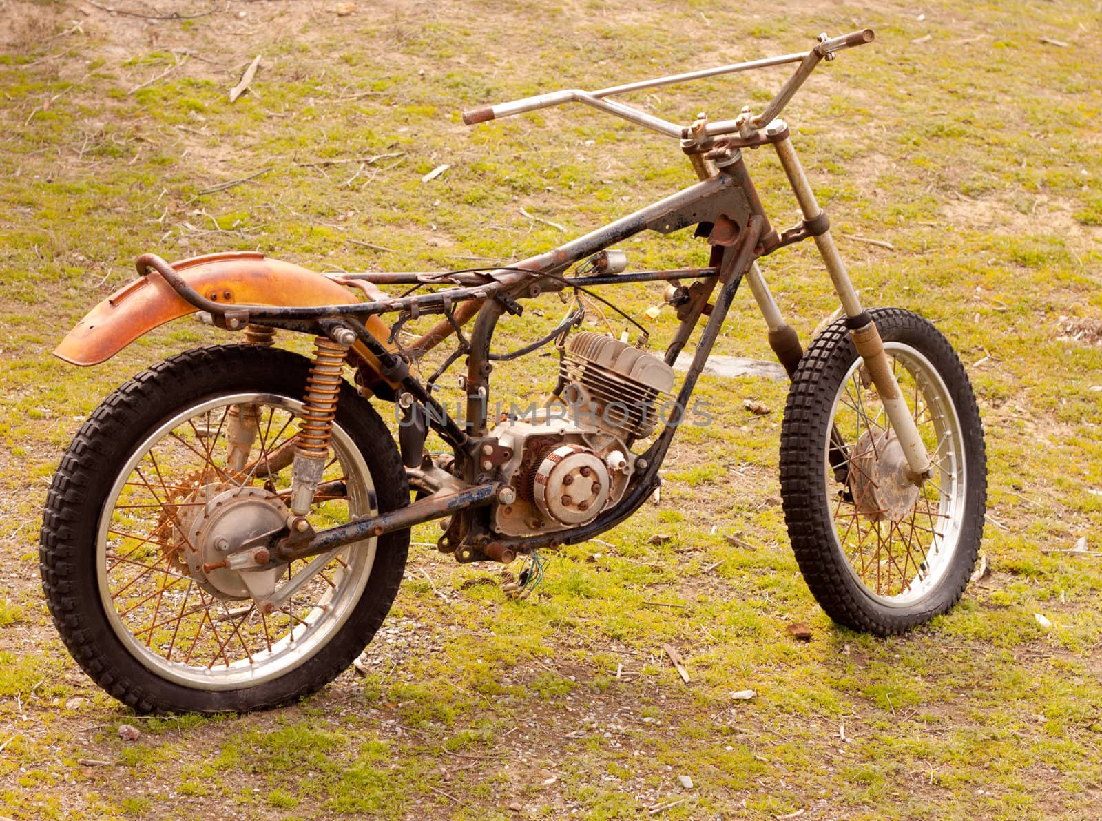 An old dilapadated motorcycle.  The motorcycle is parked on some weeds and grass.