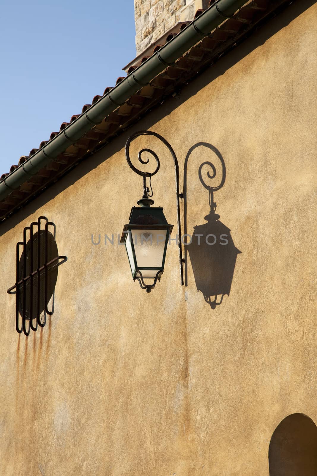 Stucco building and old lantern in sunlight with shadow.
