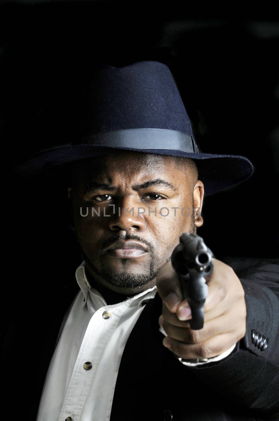 young bearded African American man pointing a revolver at the camera on a black background