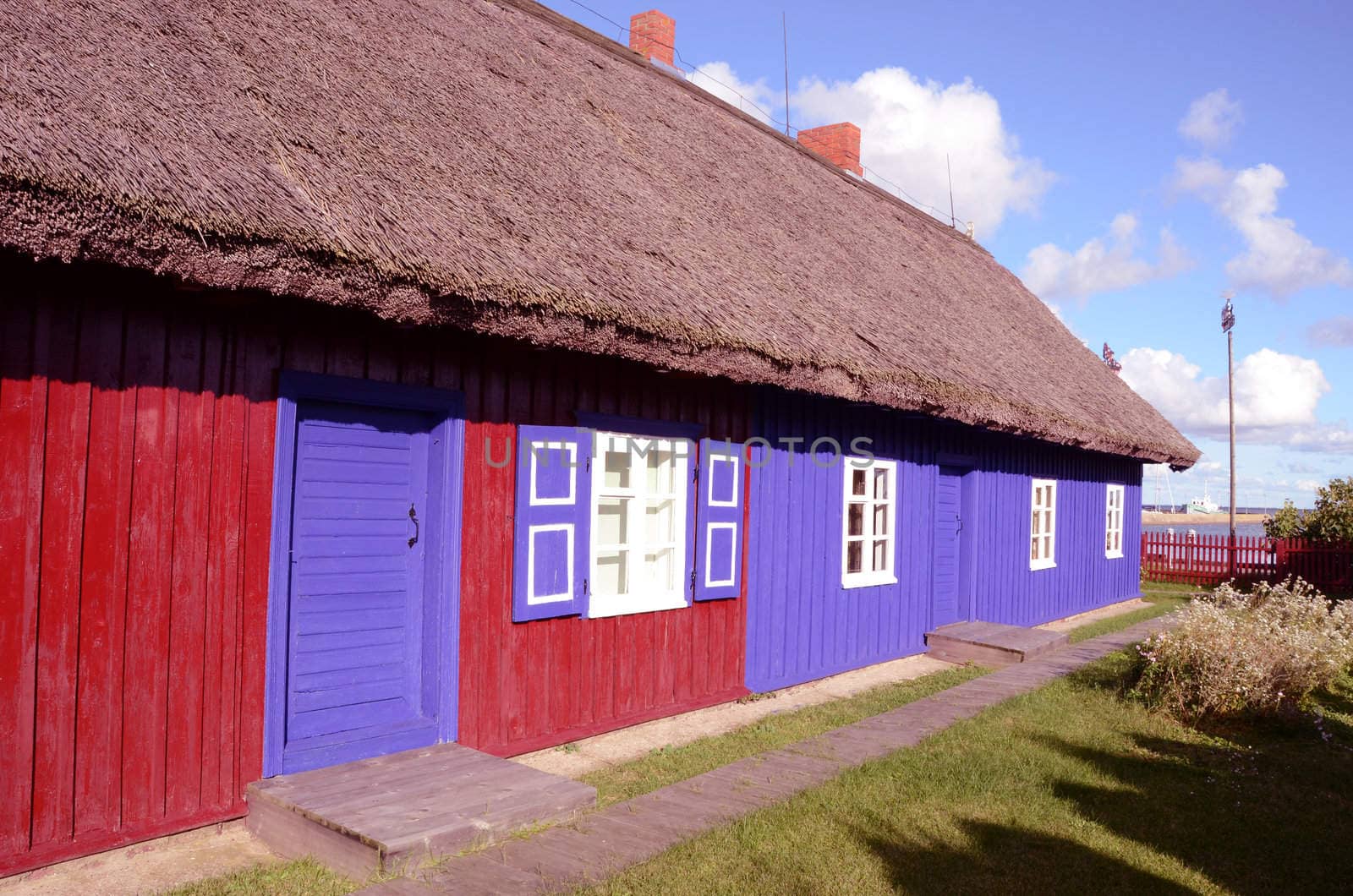 Old living house with thatch roof. Red blue painted walls. Beautiful architectural solution.