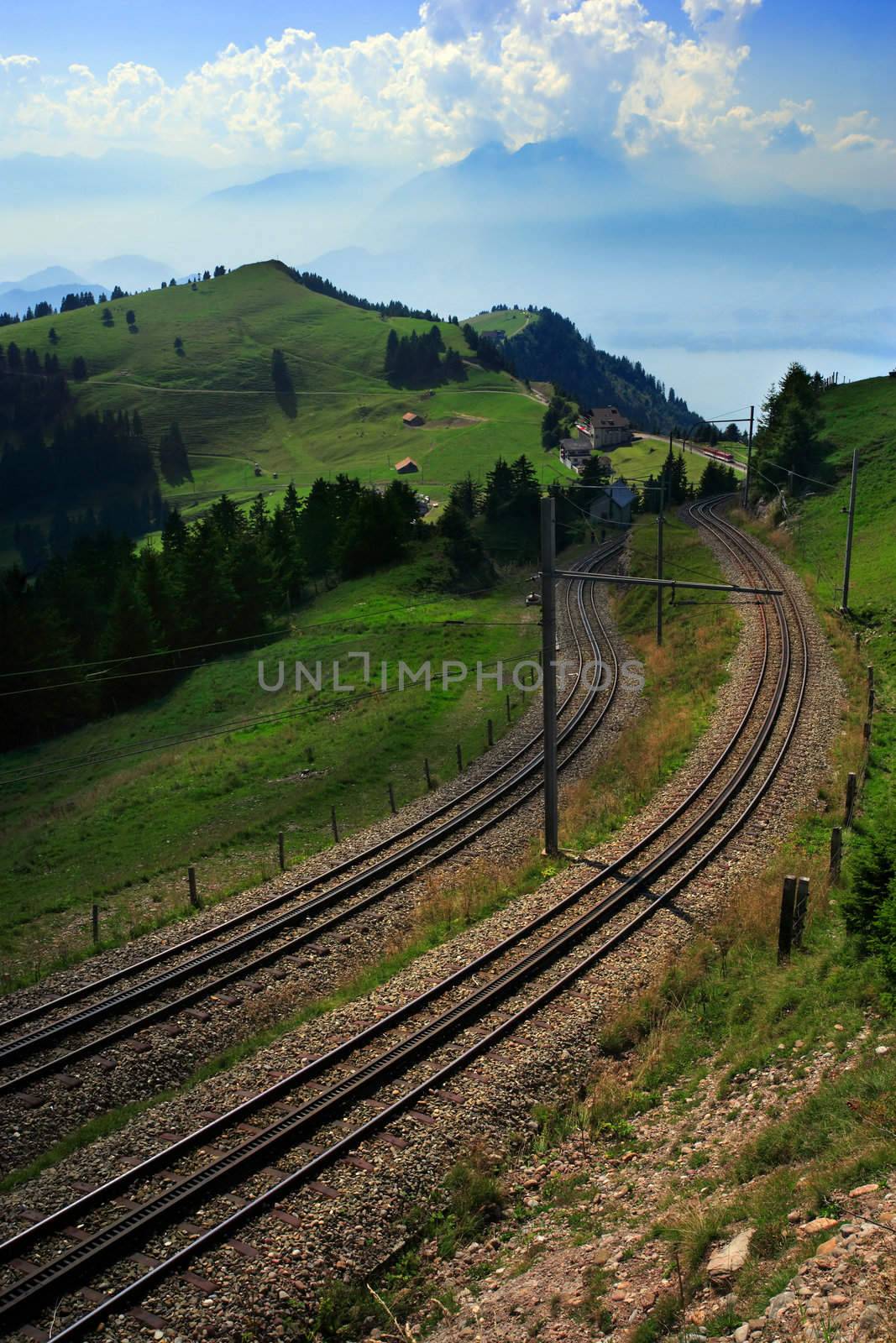 The winding tram tracks on Rigi mountain in Switzerland.  In the distance through the haze and clouds is a lake and more Alps.
