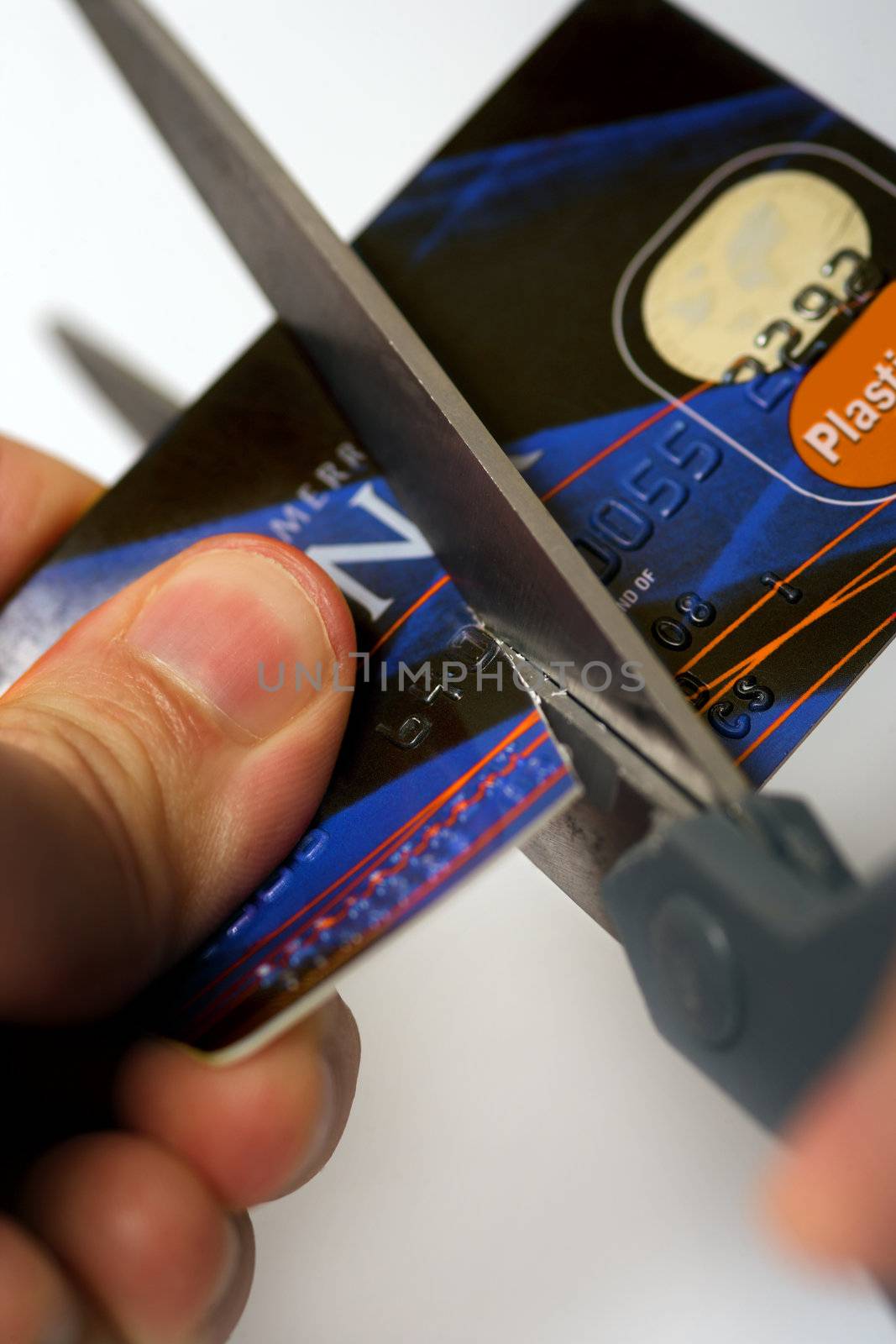 Macro image of scissors cutting through a credit card.  Logos are fake and numbers have been changed.  Colours of the card have been altered also.
