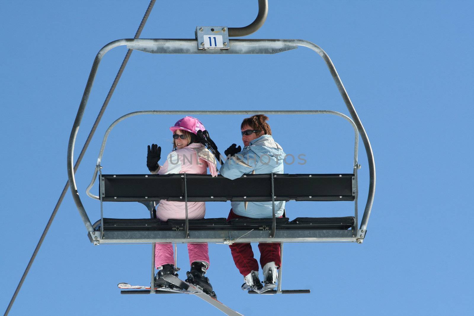 Two women wave from up on the Ski lift.