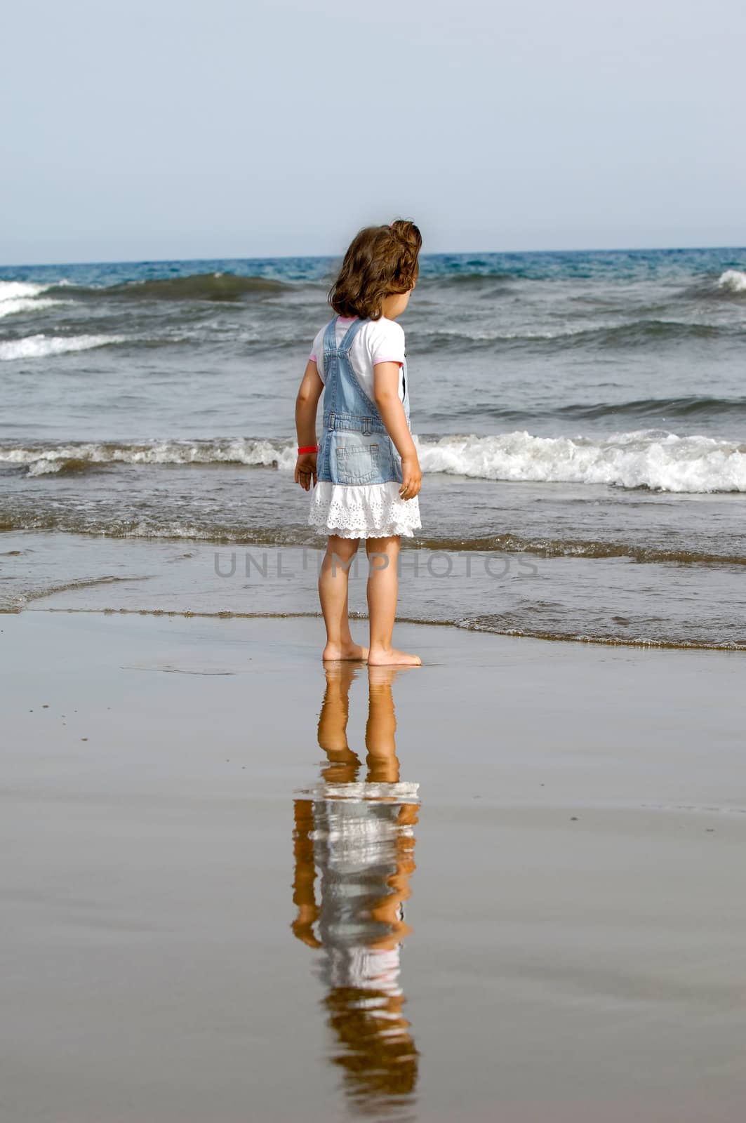 Child is standing on the beach looking at the sea.