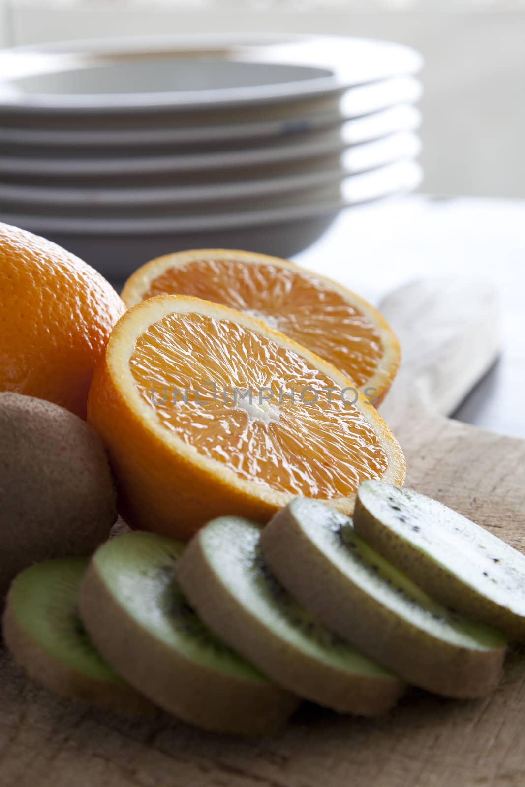 Slices of fresh kiwi fruit and orange halves on cutting board.