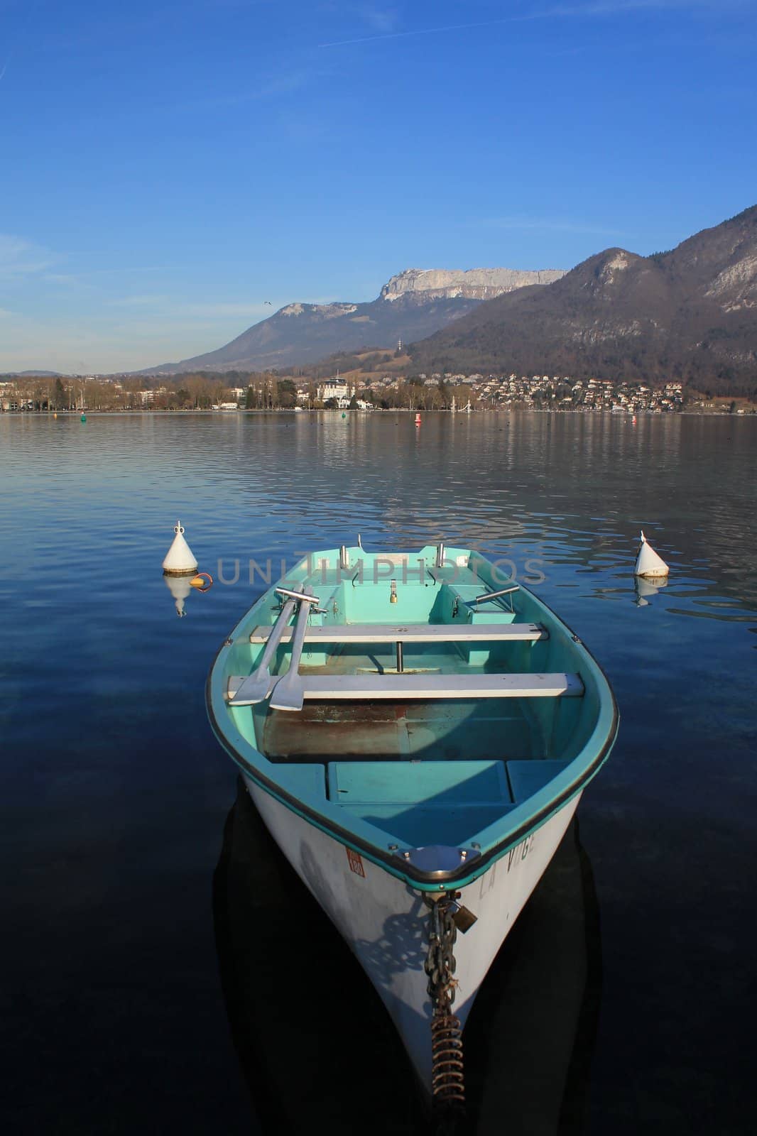 Green and white small wood boat on the Annecy lake, France, with Alps panorama by beautiful weather