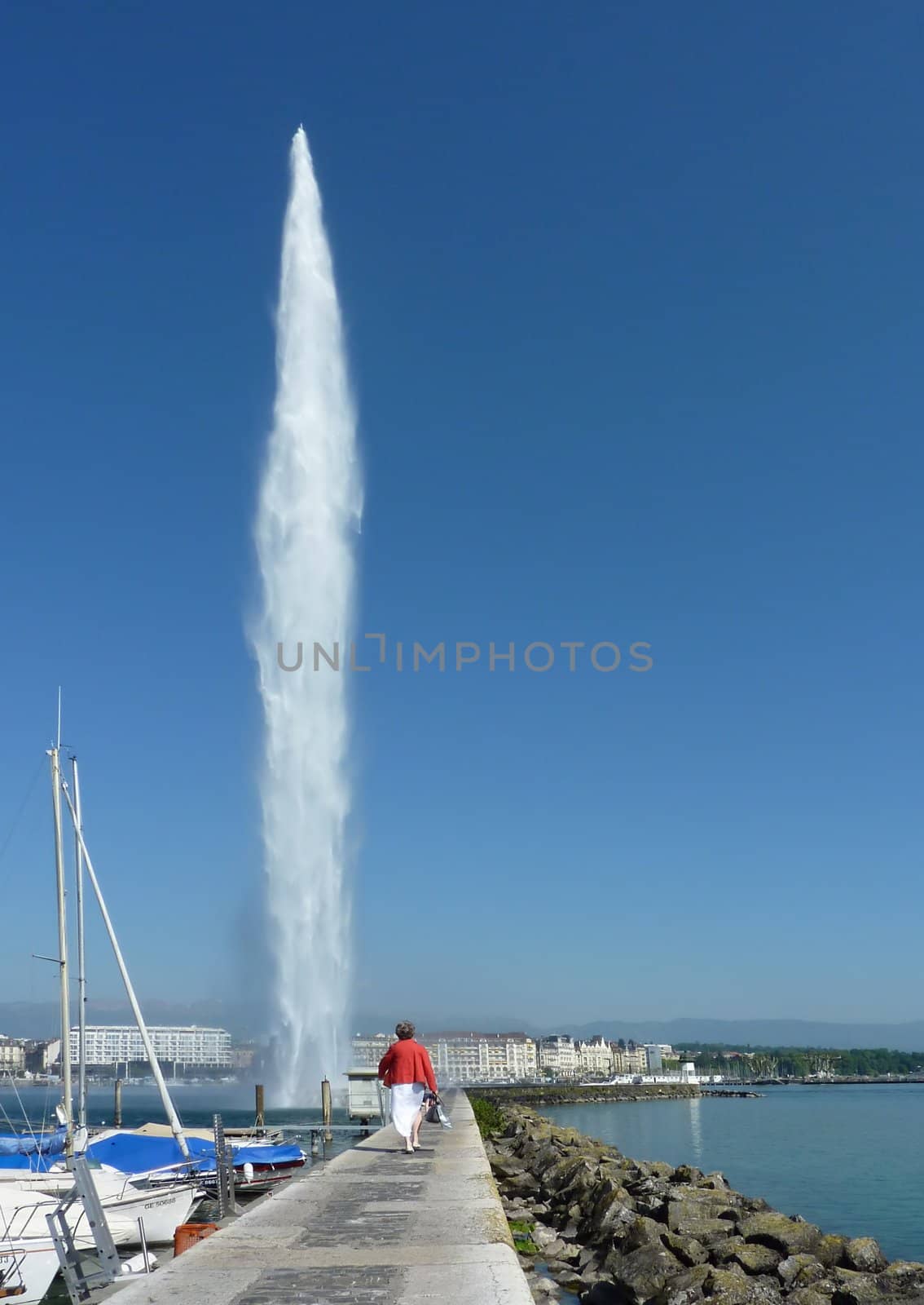 Woman wearing red cloth and walking to the famous fountain water jet in Geneva, Switzerland, by beautiful weather