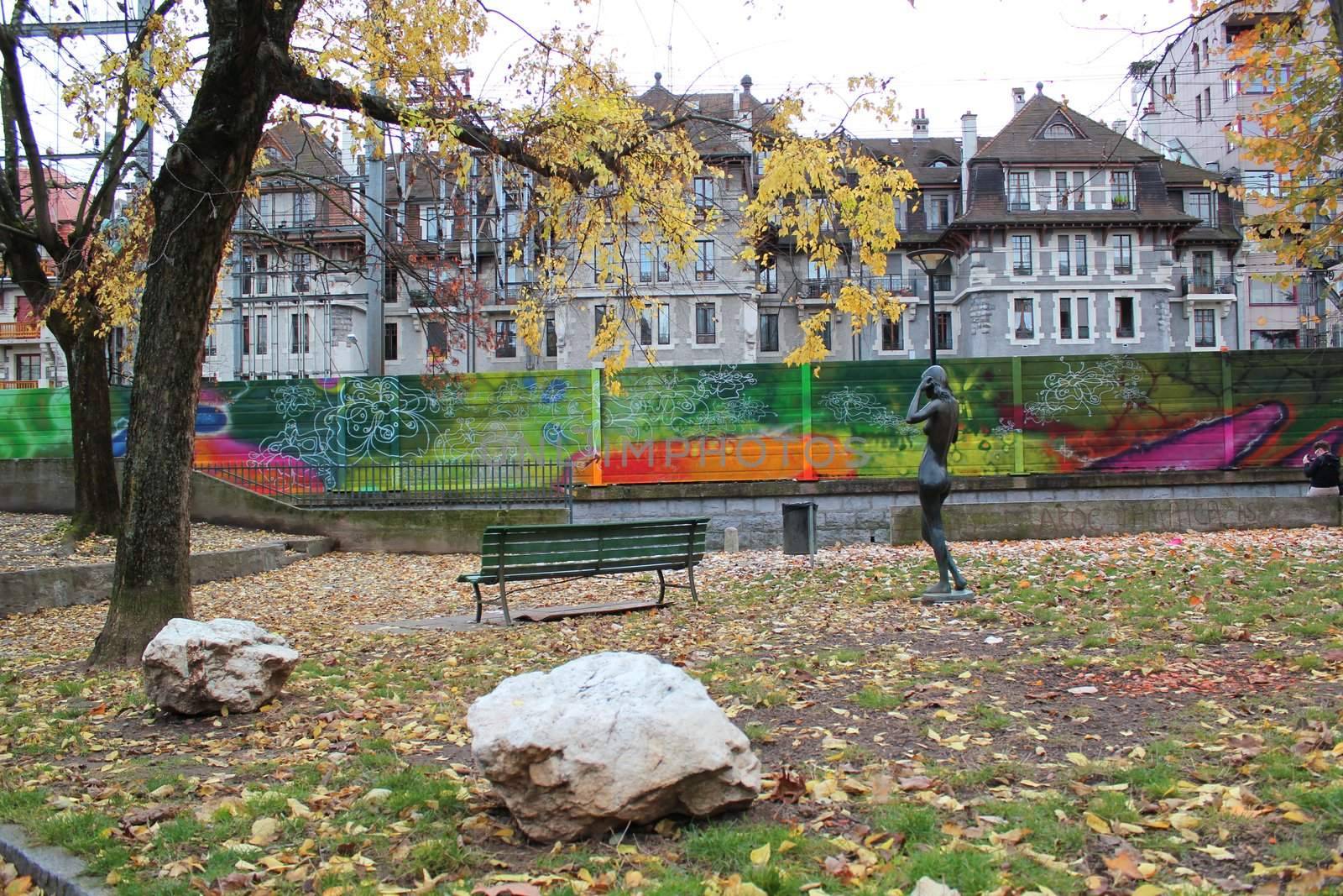View on a city park with big stones, trees, yellow leaves, a statue, graffities and buildings by autumn weather