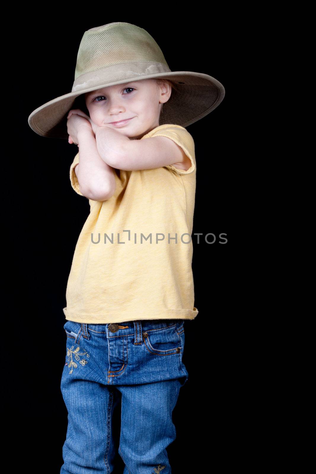 A girl with an oversized hat on.  Her arms and hands are clasped behind her head as if she is holding something back or hiding something.