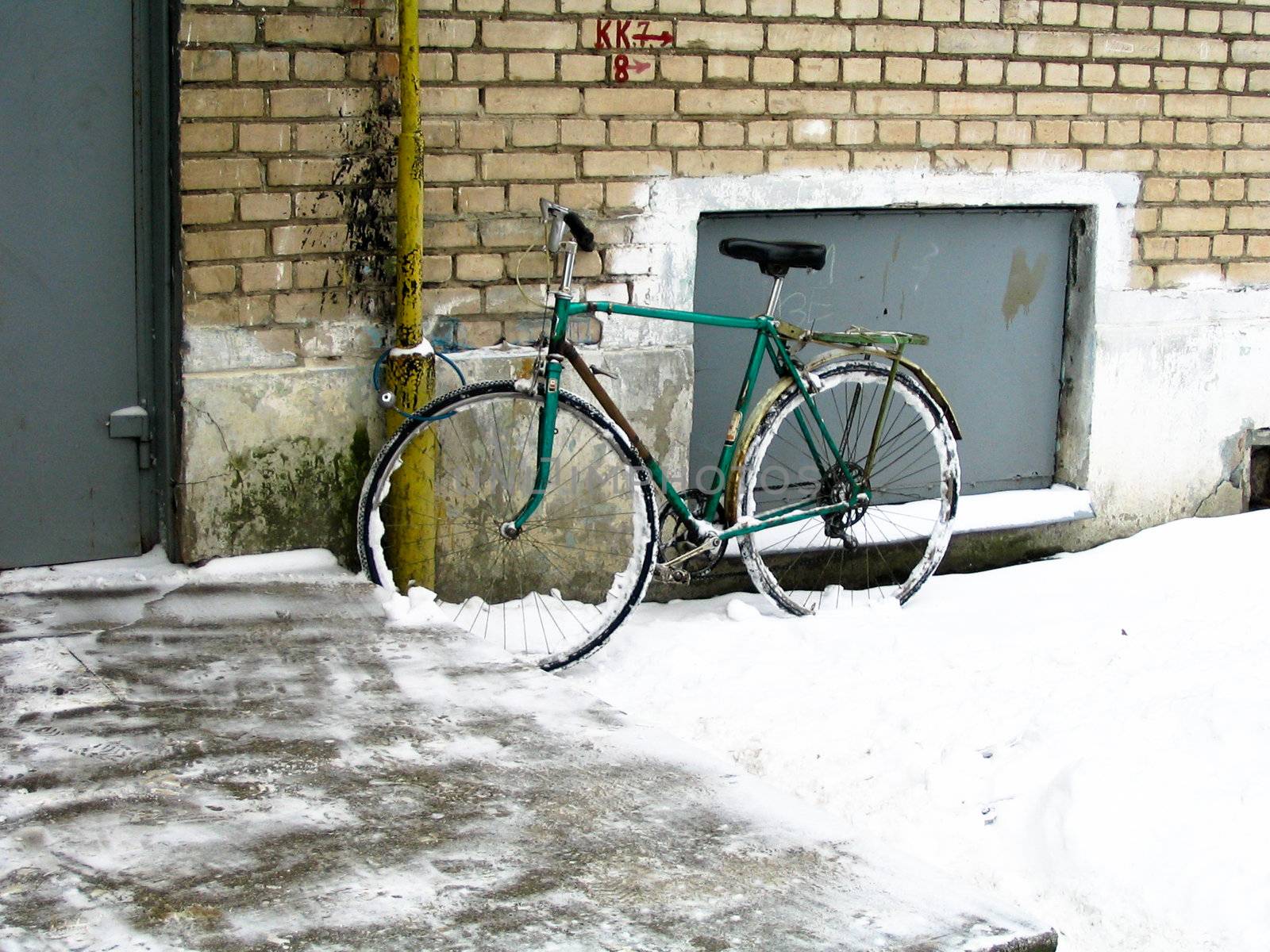 The bicycle standing at a wall of the brick house in the winter