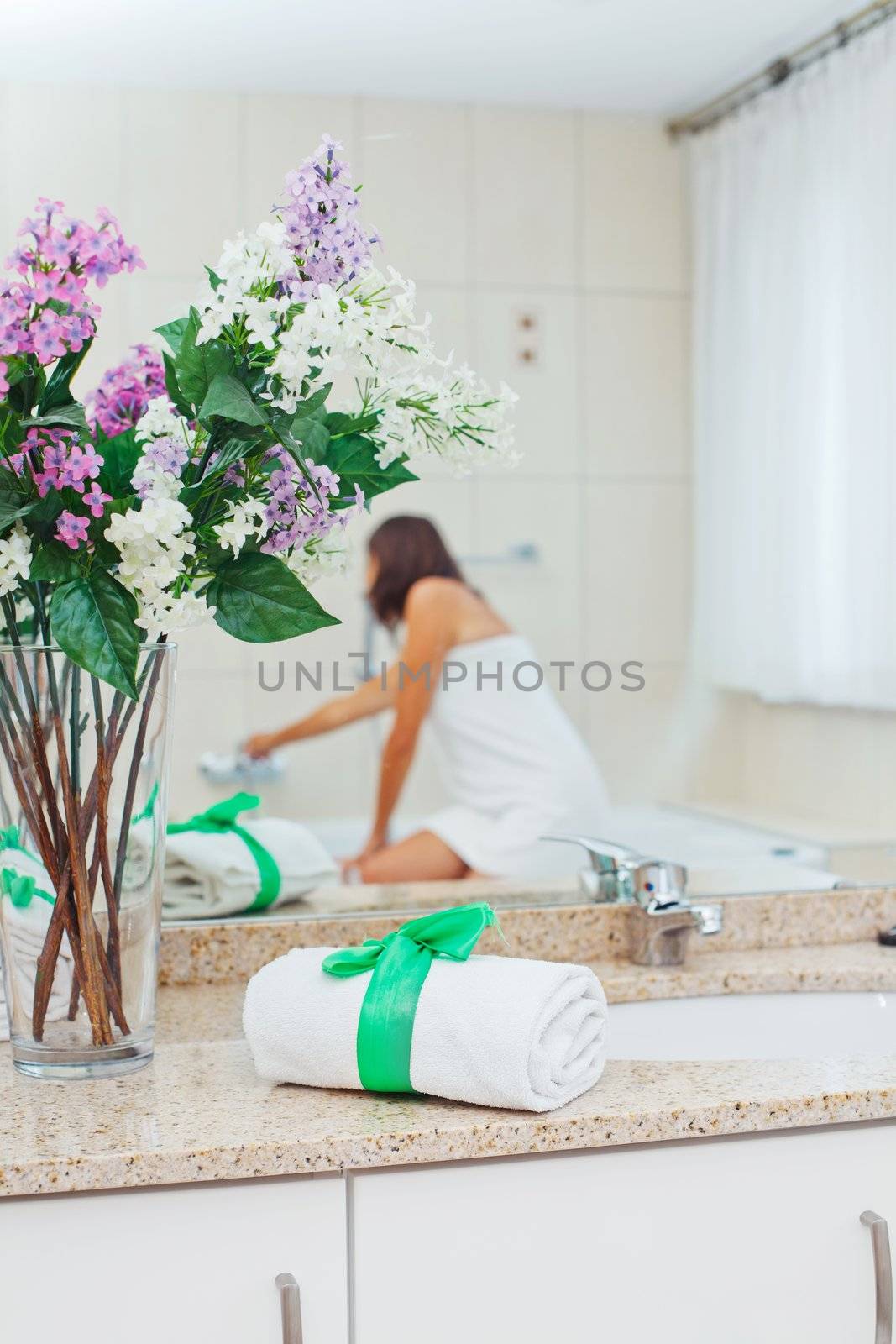 Mirror in a bathroom with rolled up towel next to it and flowers