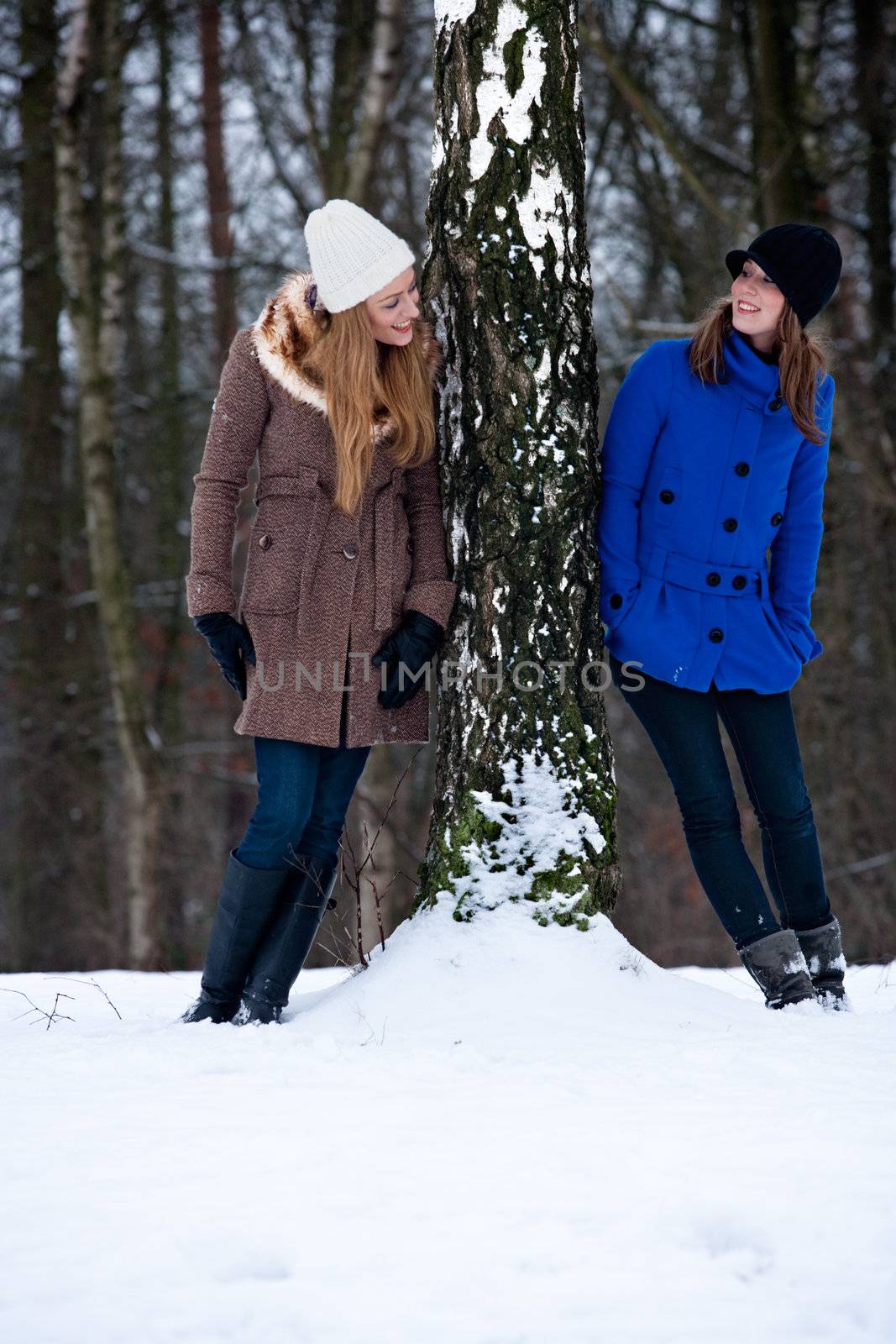 Two sisters standing on each side of a tree in winter