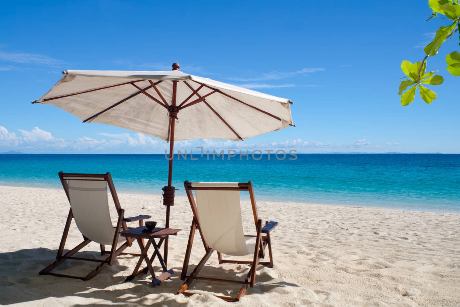 Deckchairs and parasol on the white sand beach facing the lagoon