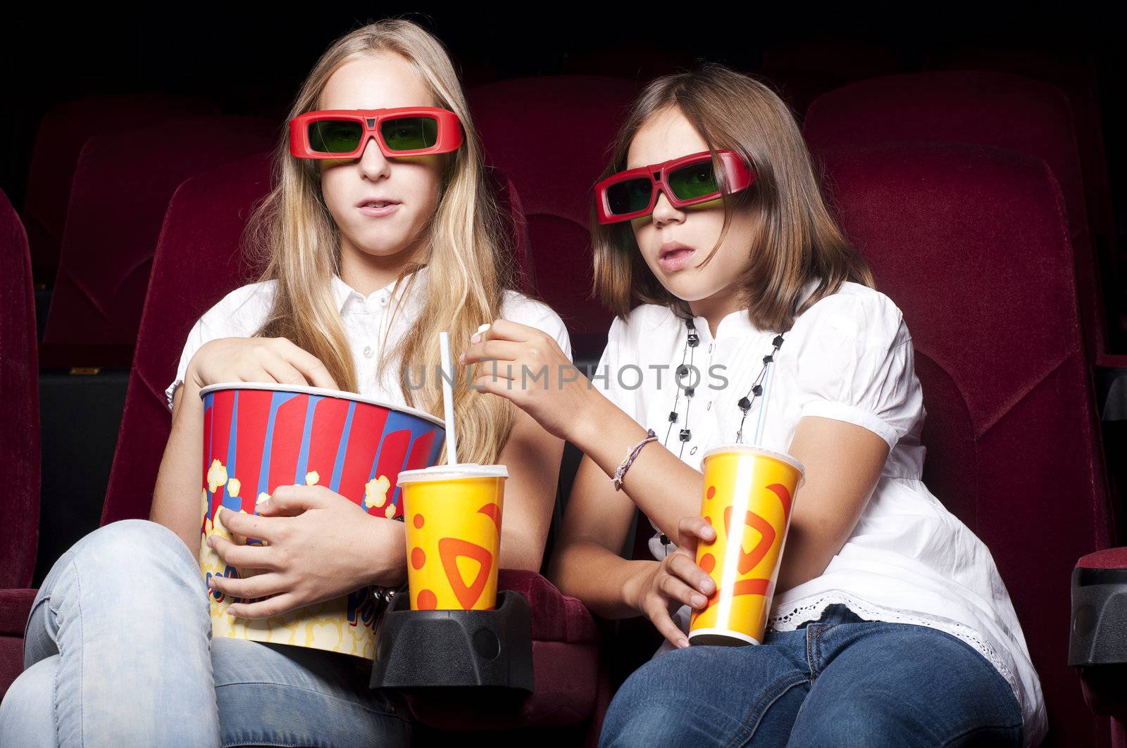 two girls look three-dimensional cinema, sitting in the glasses, eat popcorn, drink drink