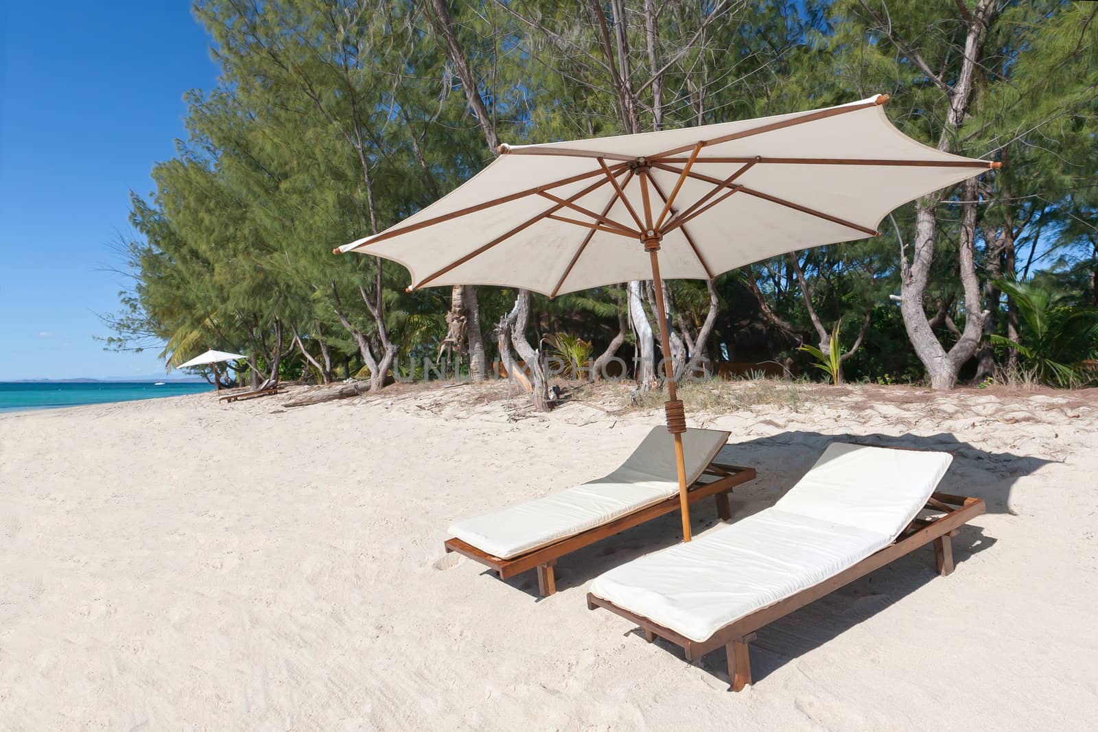 Deckchairs and parasol on the white sand beach facing the lagoon