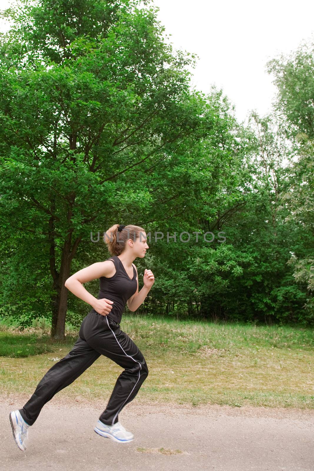 Sportive young woman running over a forrest road by DNFStyle