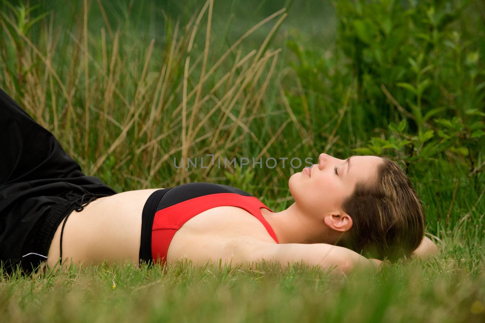 Sportive young adult resting in the grass of a meadow by DNFStyle