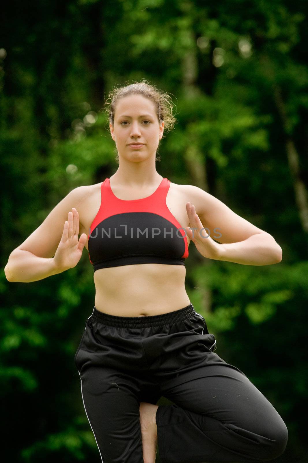 Young adult woman practising yoga on a field surrounded by trees