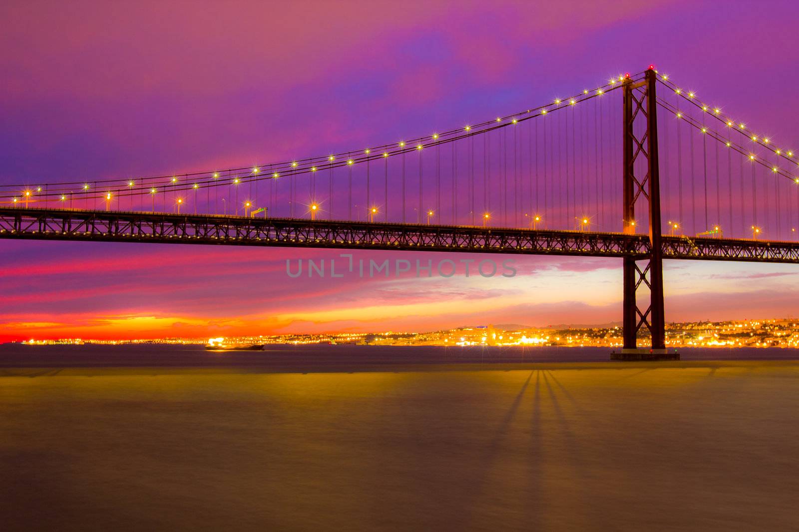 The 25 de Abril Bridge - suspension bridge over the river Tagus illuminated at night. Lisbon Portugal