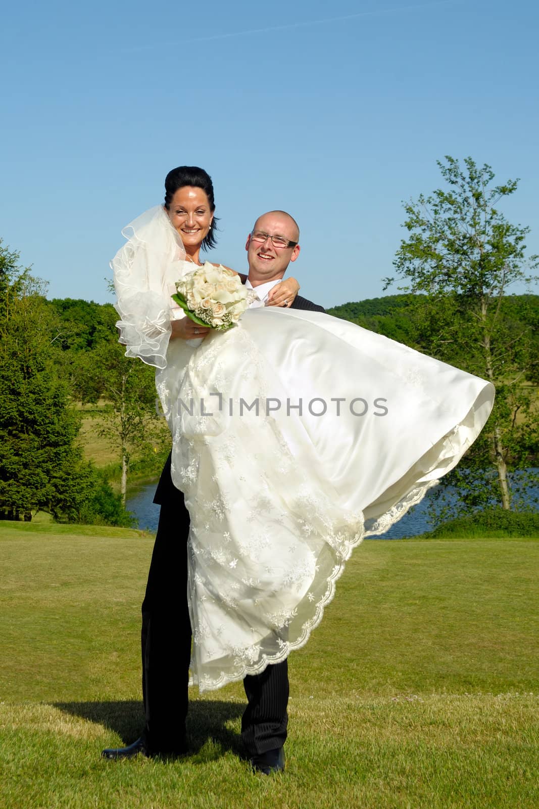 Groom is lifting his bride up in a park.