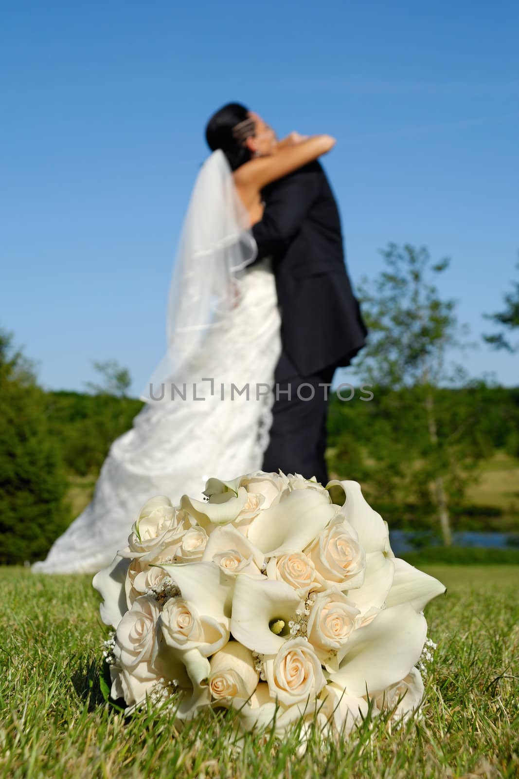 Wedding bouquet in focus and couple in the background holding each other.