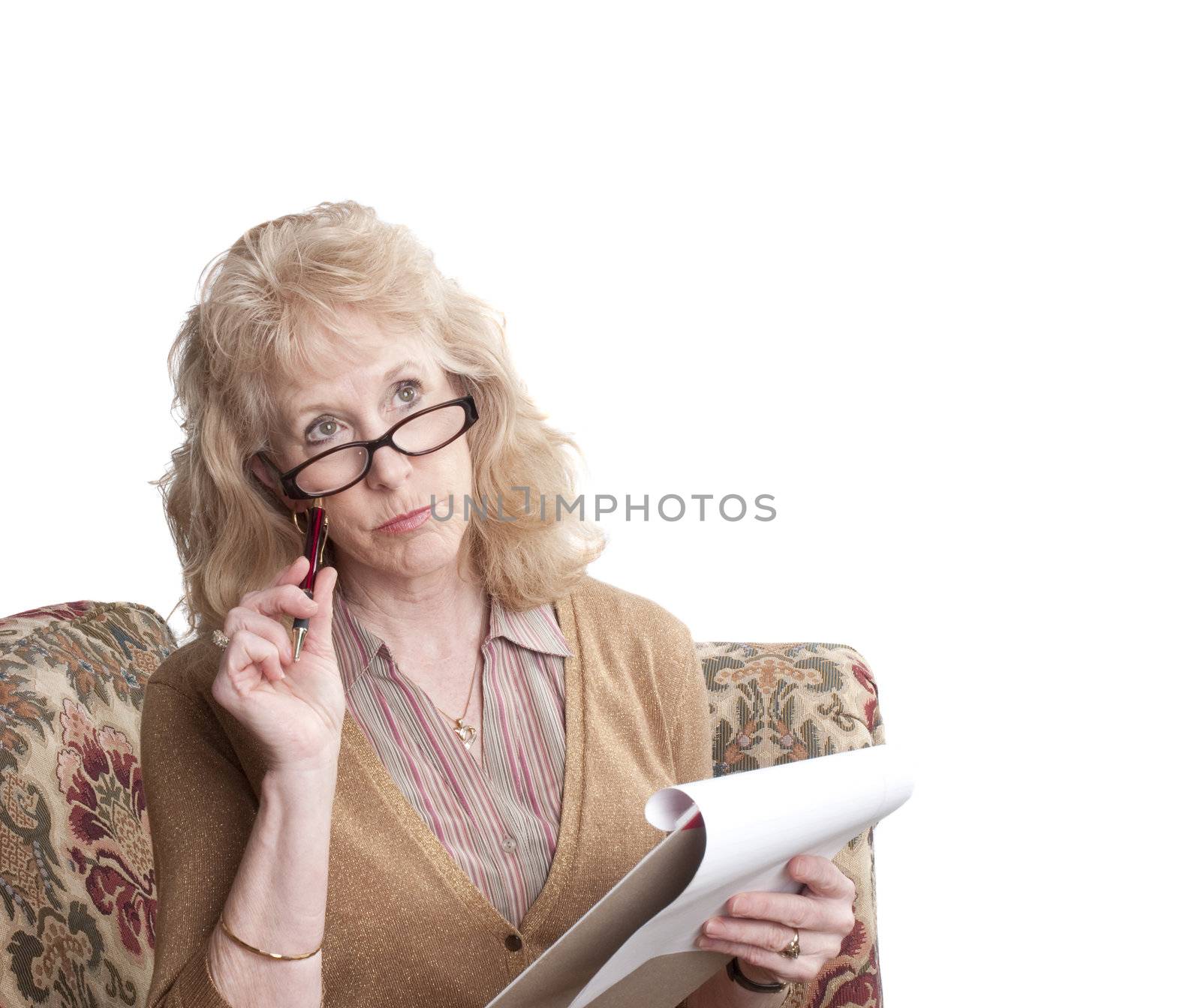 middle-aged woman with glasses on, sitting on sofa with note pad looking perplexed,  isolated on white