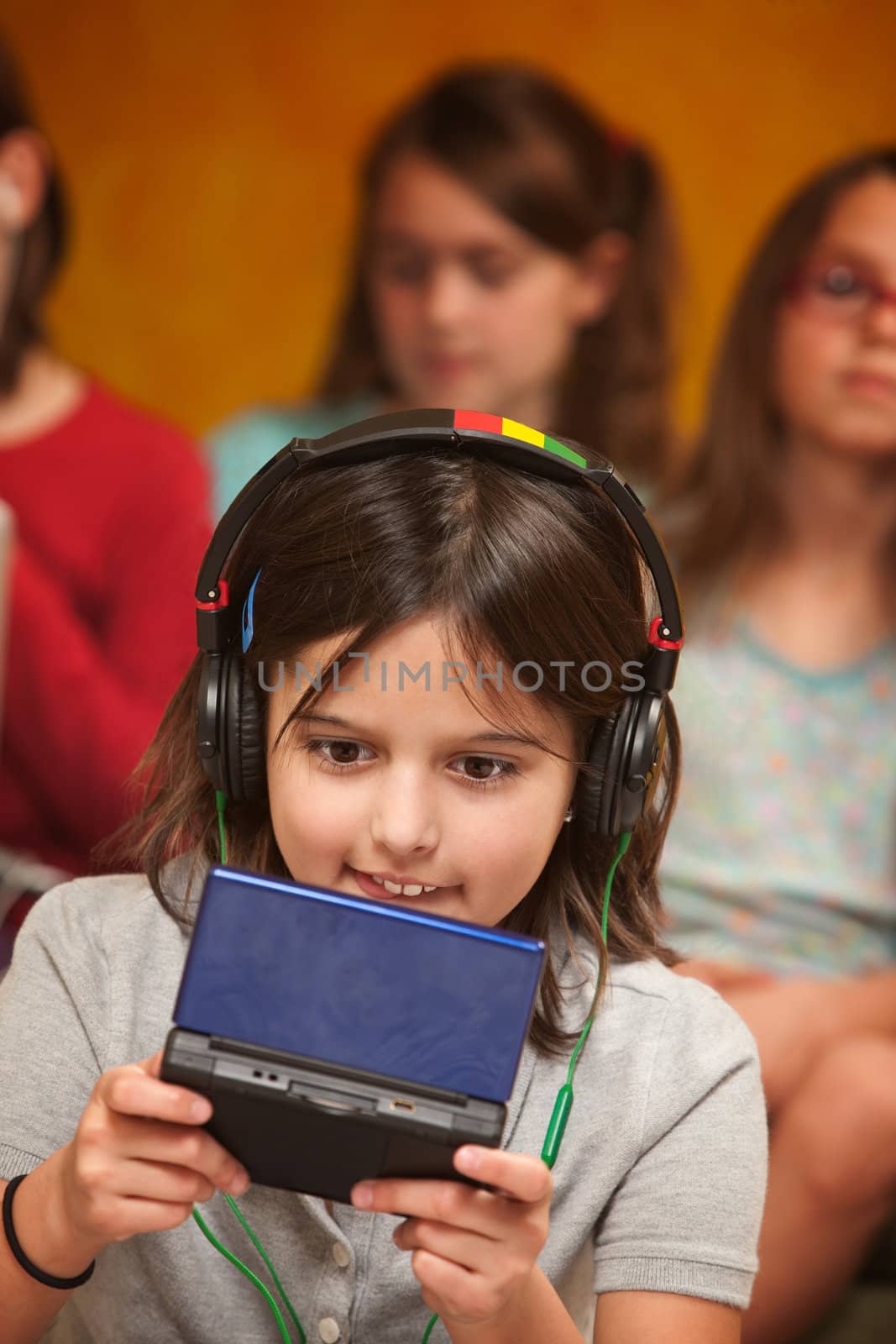 Little Caucasian girl with earphones plays a handheld video game