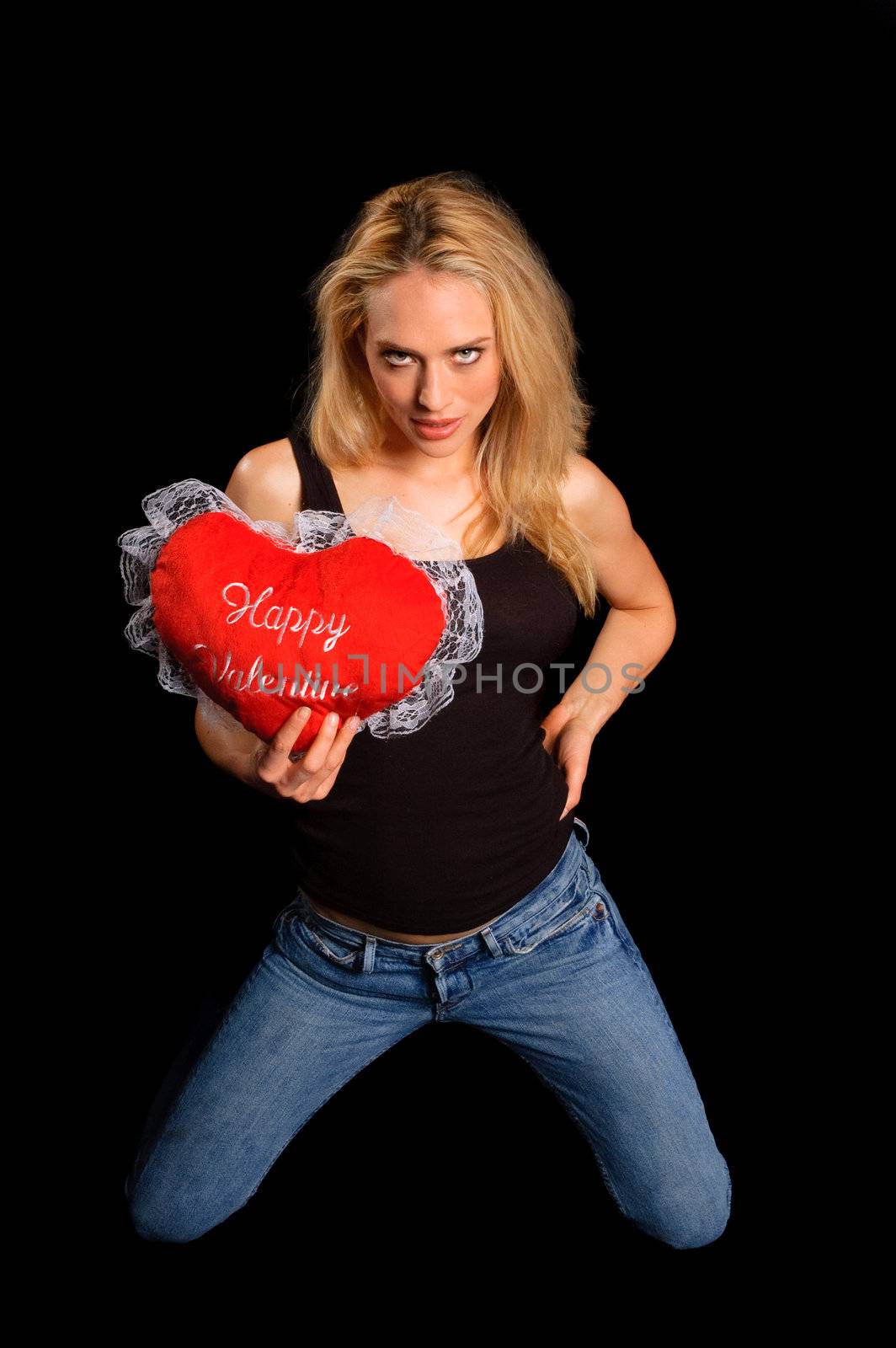 a seductive young woman in blue jeans kneeling while holding a red pillow which has Happy Valentine on it.