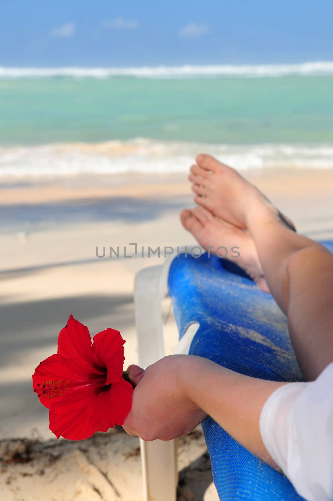 Young woman relaxing on a tropical beach holding a red flower