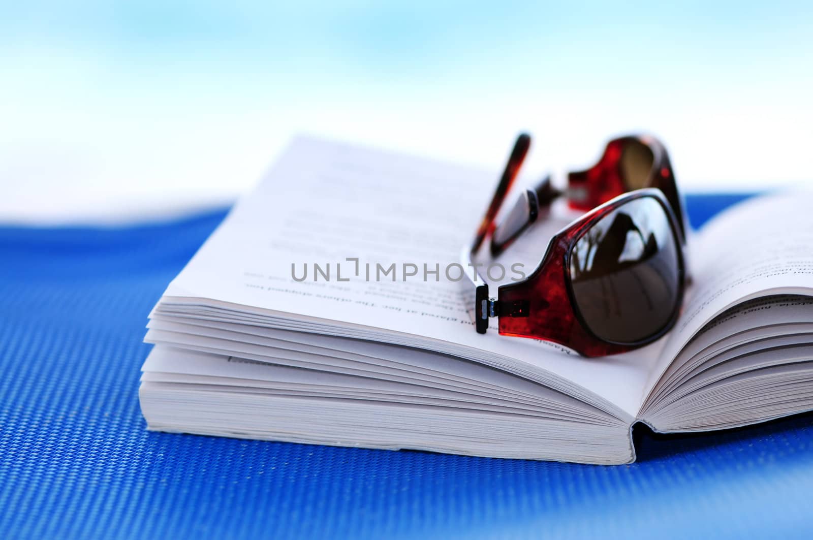 Sunglasses and open book on beach chair - summer vacation concept
