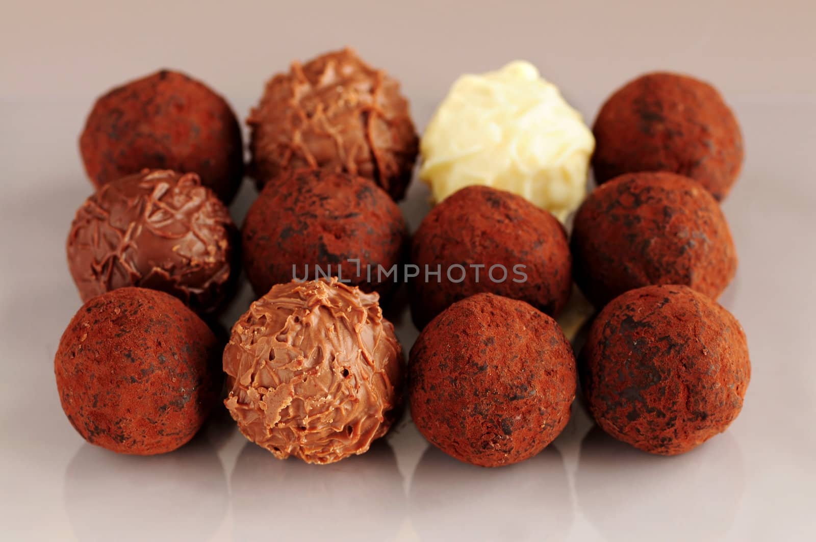 Several assorted chocolate truffles in rows on brown background
