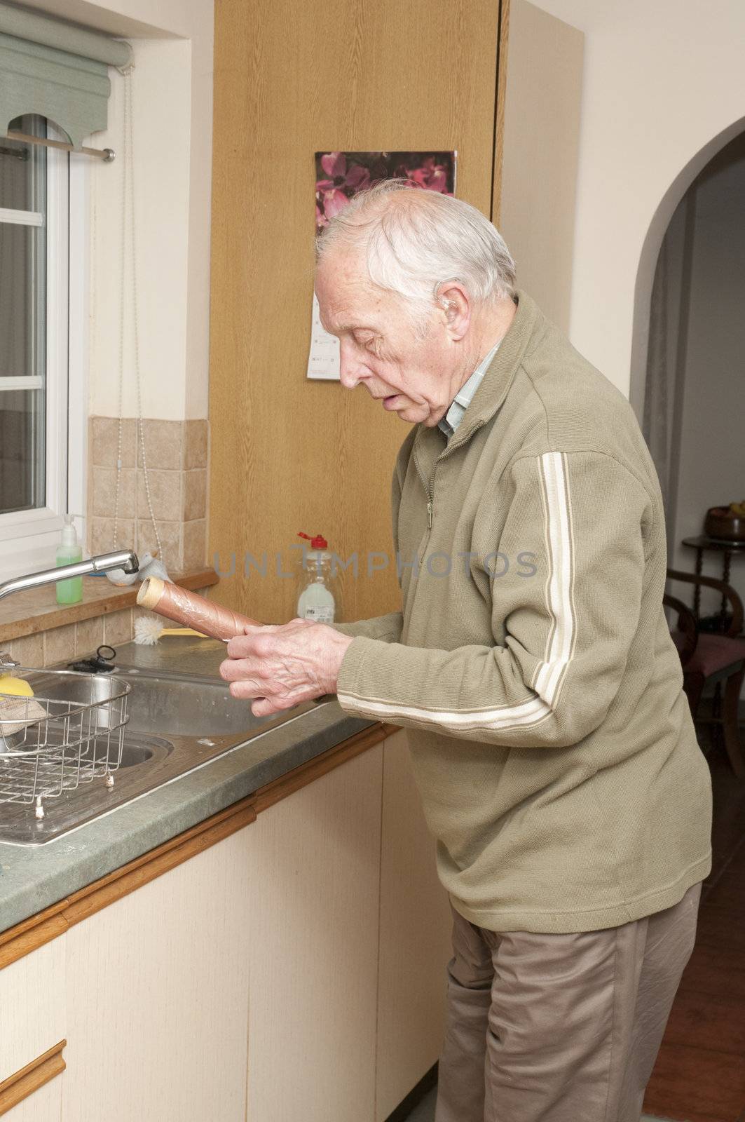 Elderly man with hearing aid working in kitchem