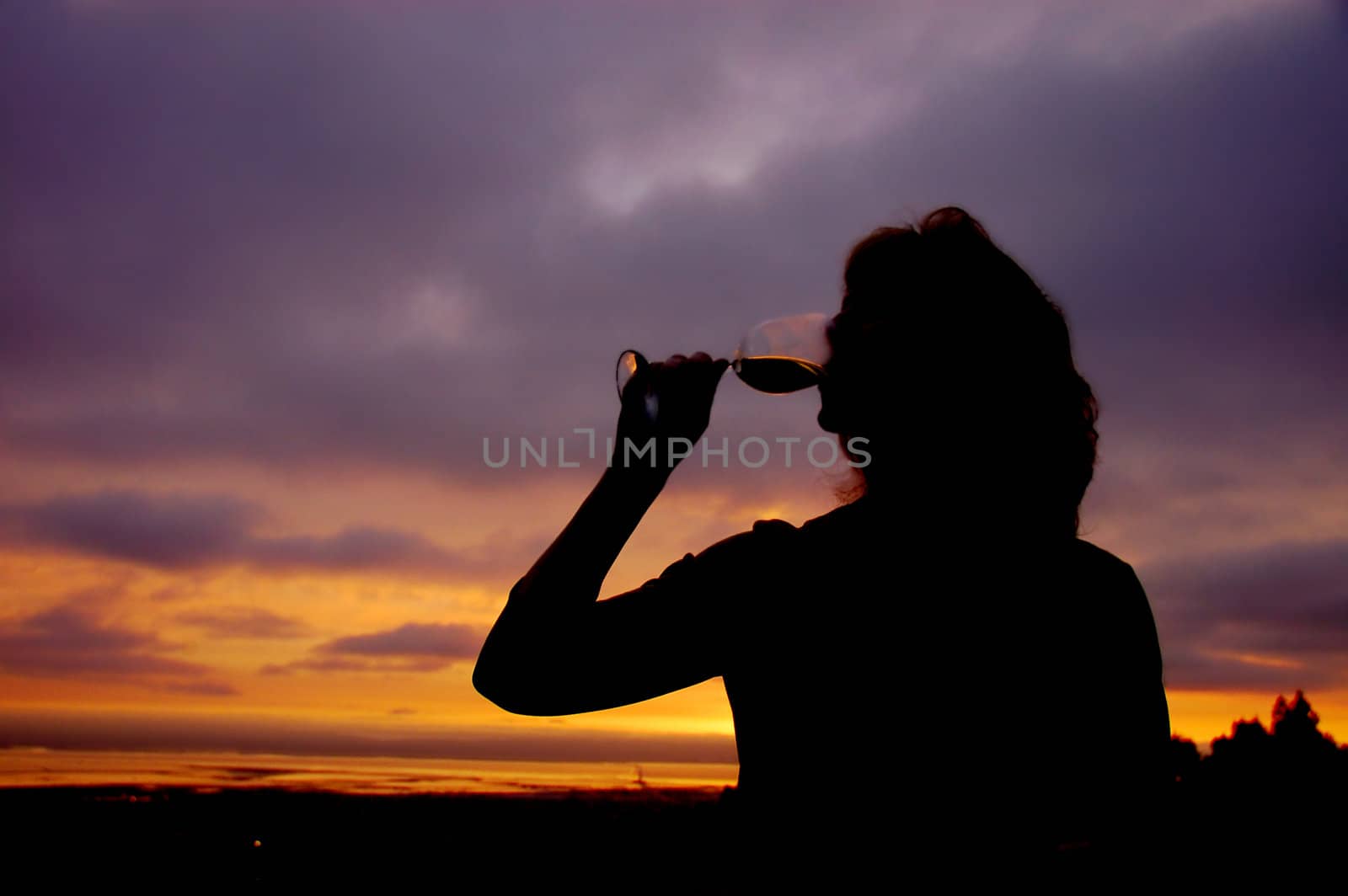 Beautiful middle aged woman drinking a glass of wine on her deck at sunset