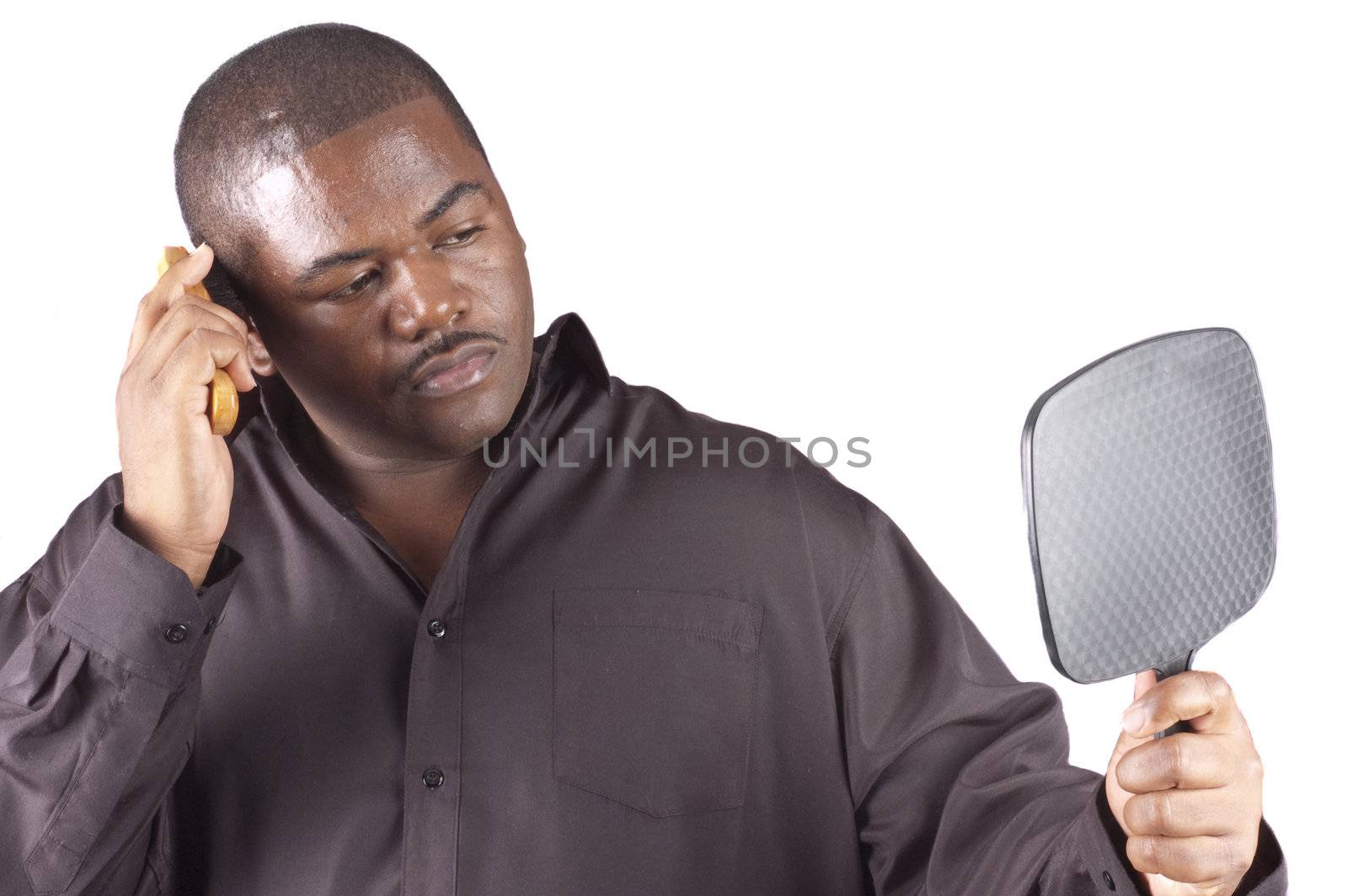 young african man preening, grooming his hair, holding a mirror in front of him and over a white background