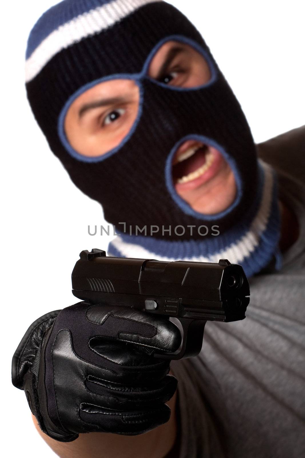 An angry looking man wearing a ski mask pointing a black handgun at the viewer. Shallow depth of field with sharpest focus on the gun.